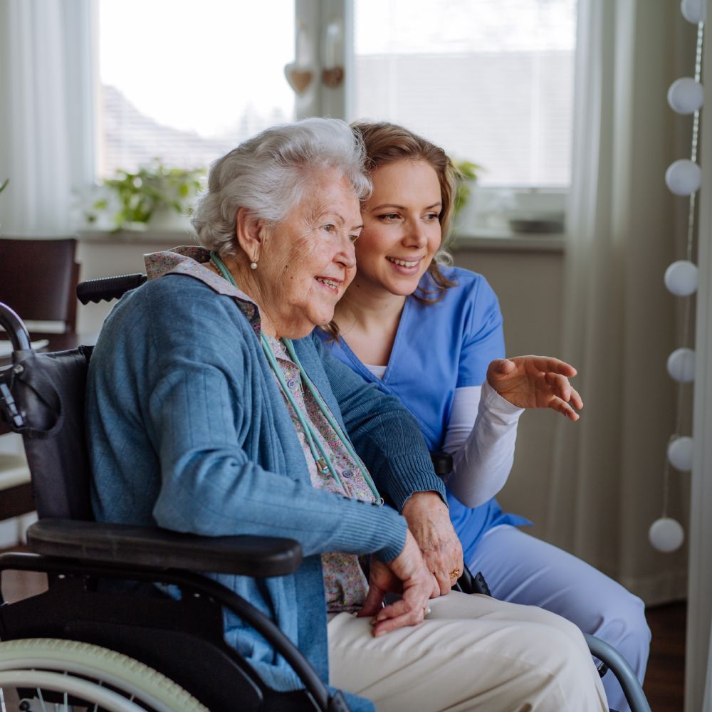 An elderly woman in a wheelchair is sitting next to a nurse.