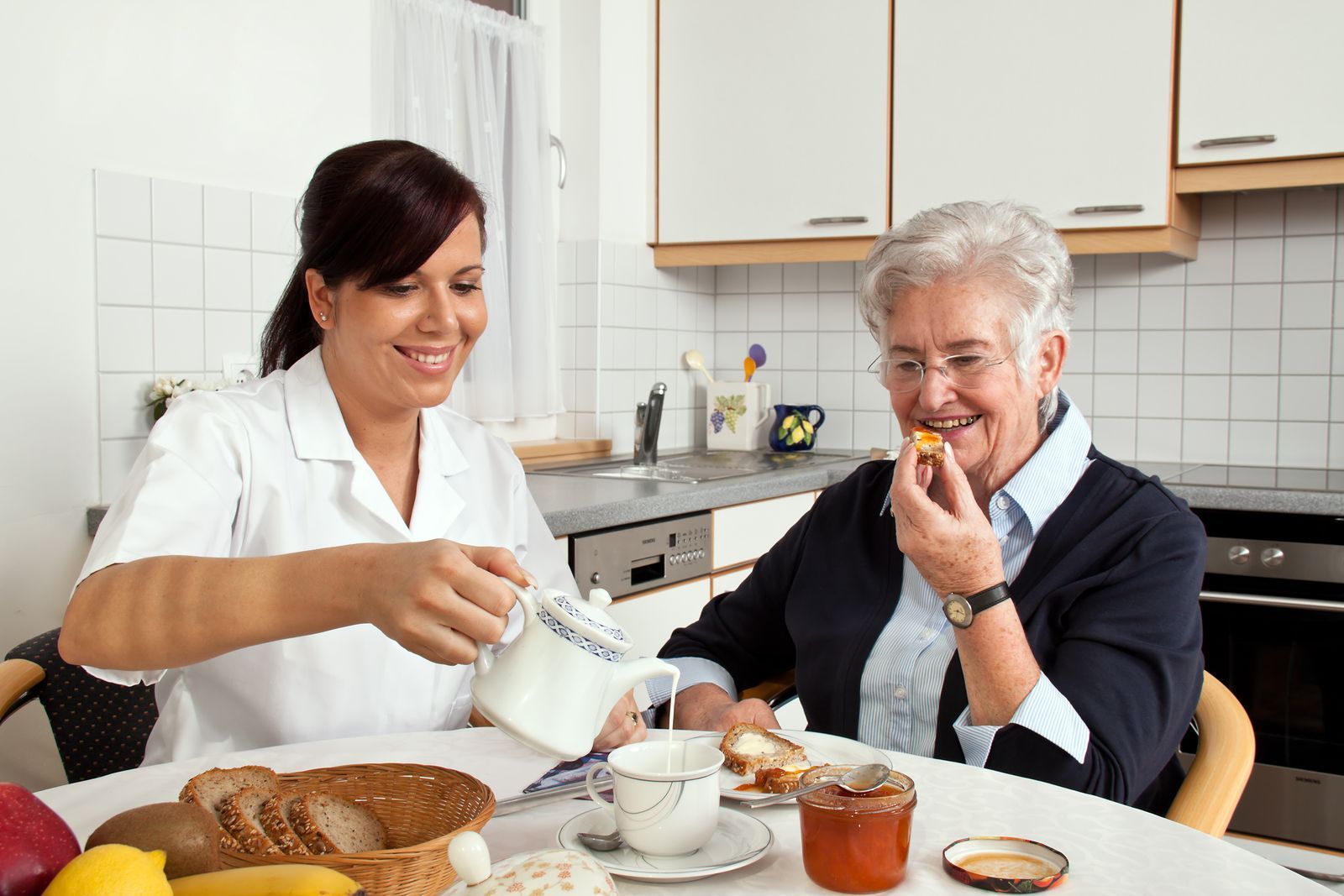 A woman is pouring tea into a cup for an elderly woman.