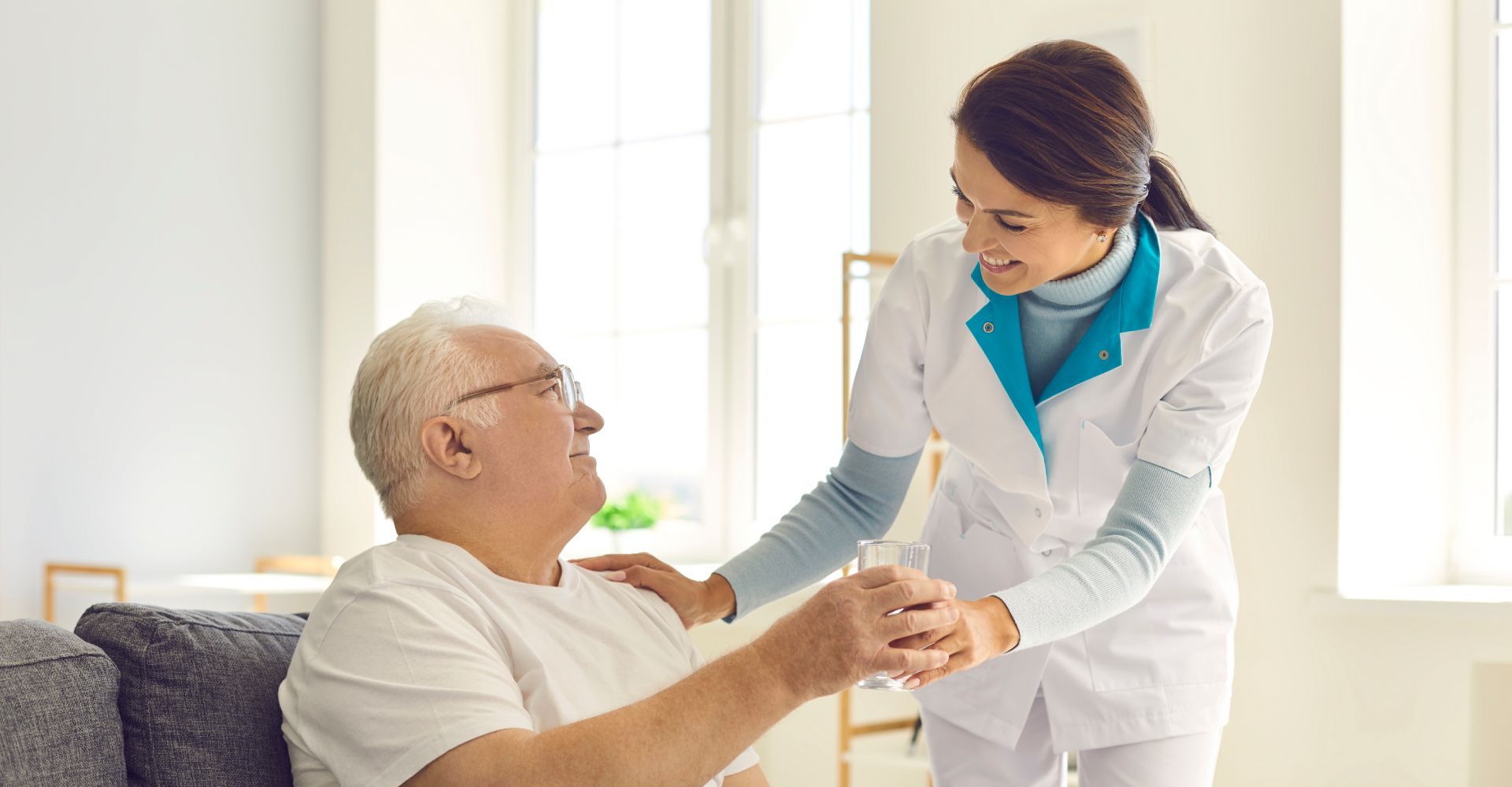 A nurse is holding the hand of an elderly man sitting on a couch.