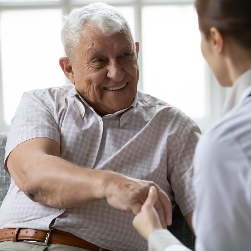 An elderly man is sitting on a couch talking to a nurse.