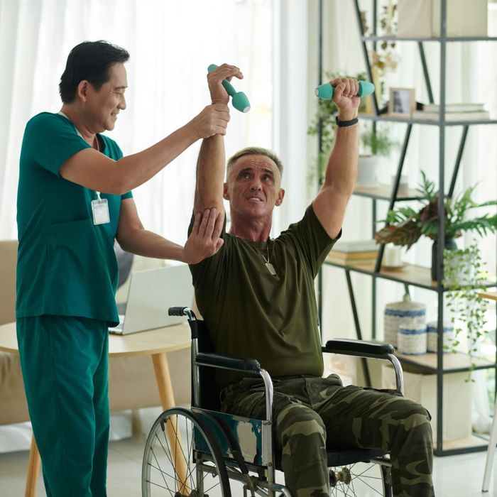 A man in a wheelchair is being helped by a nurse to lift dumbbells.