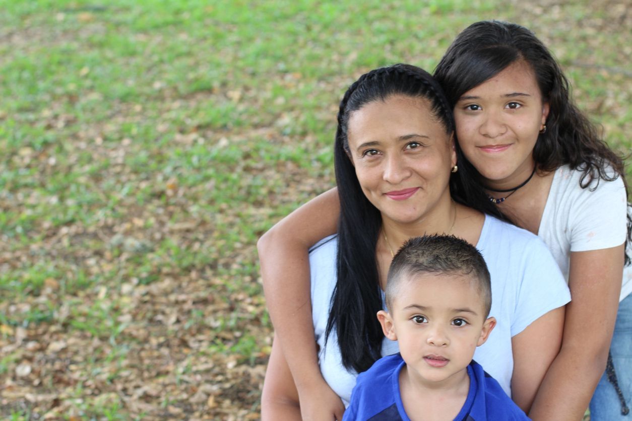 Madre y dos niños sonriendo al aire libre. Fondo de hierba verde.