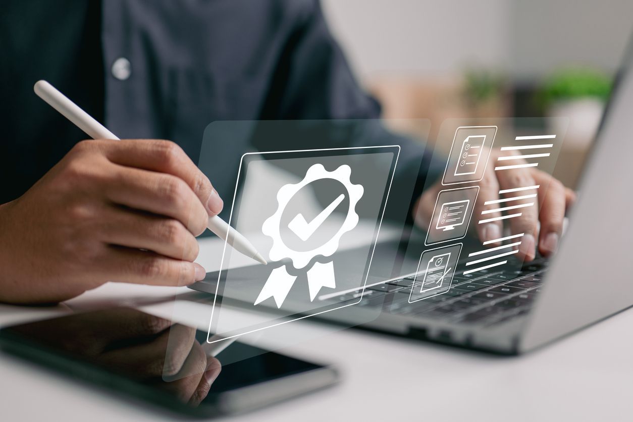 Persona que utiliza una computadora portátil y un lápiz con un sello de calidad virtual y una lista de verificación flotando encima.