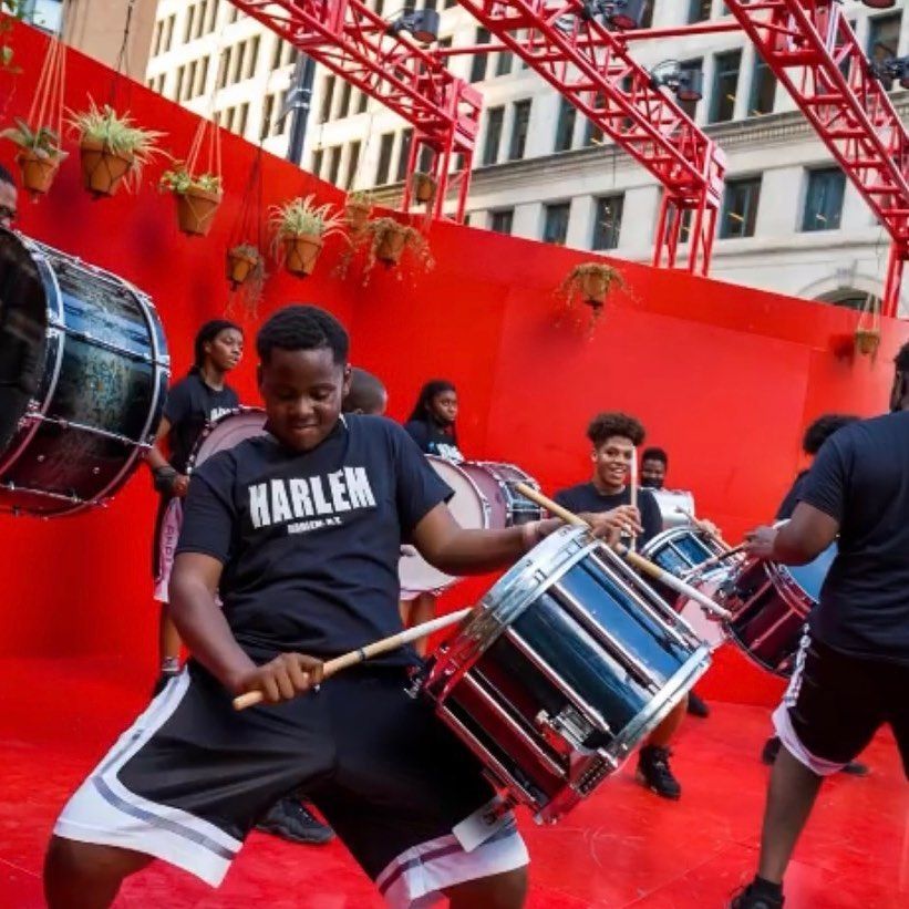 a man wearing a harlem shirt is playing drums