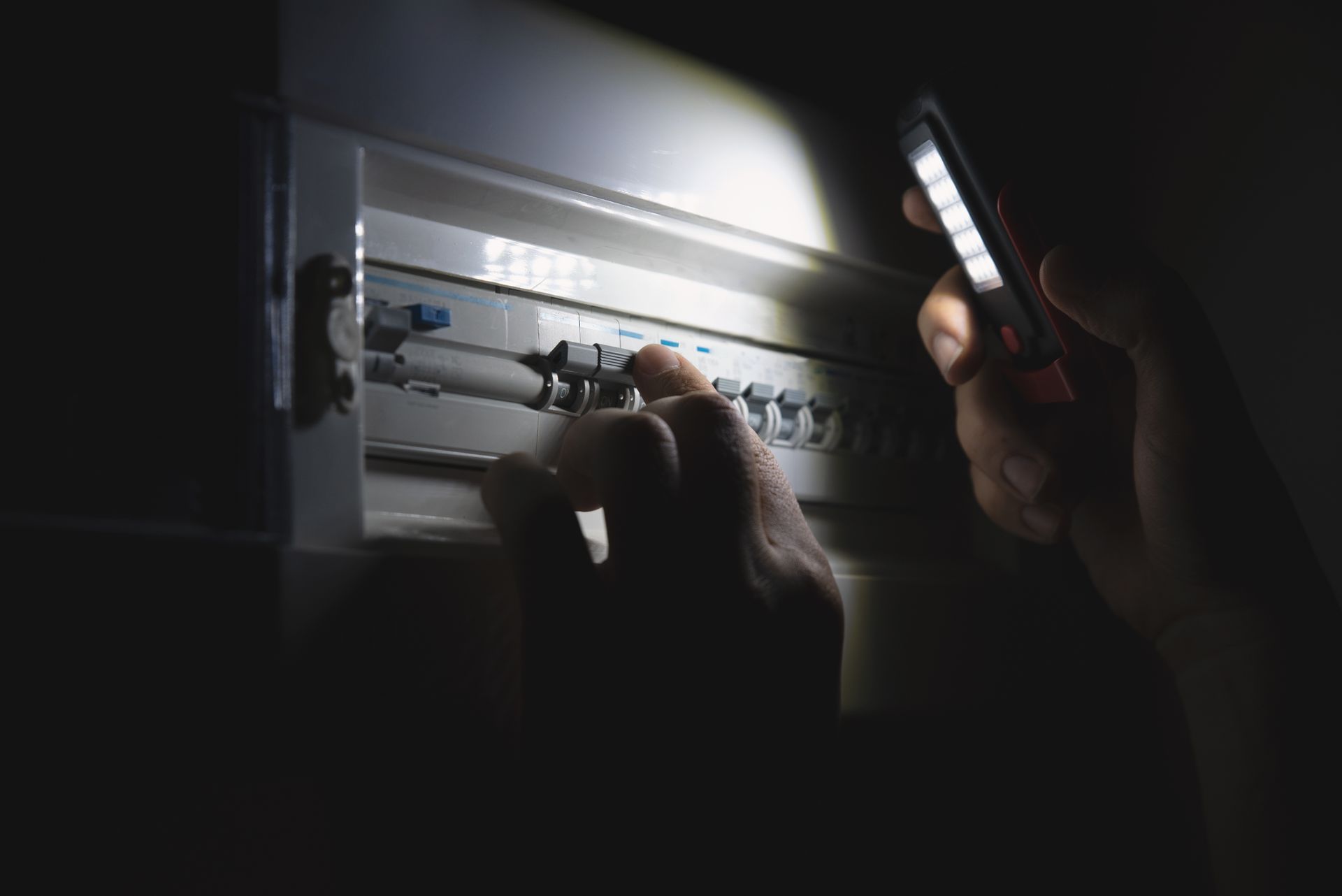 Person using a flashlight to inspect and flip switches on a home electrical breaker panel