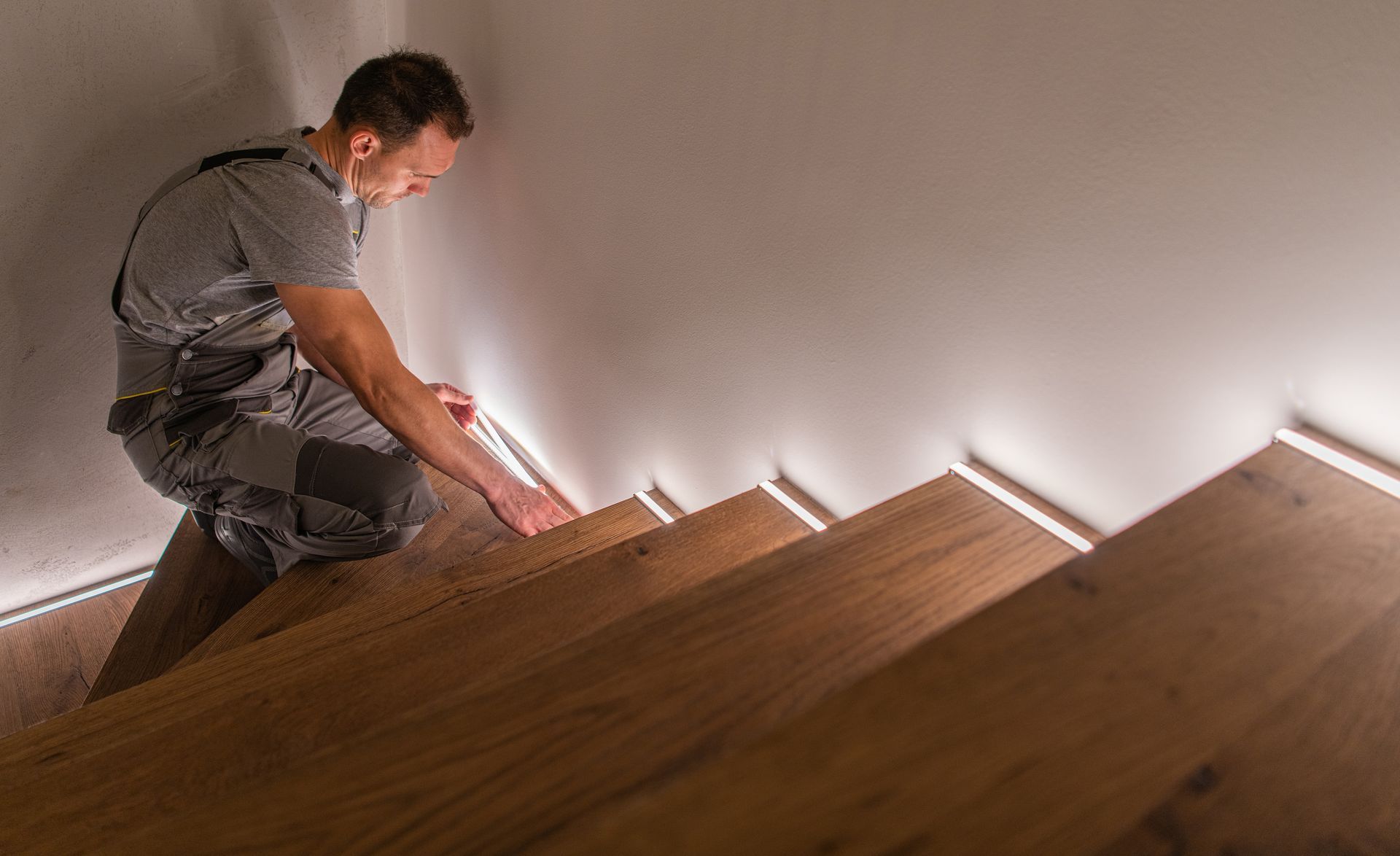 A man is kneeling down on a wooden staircase.