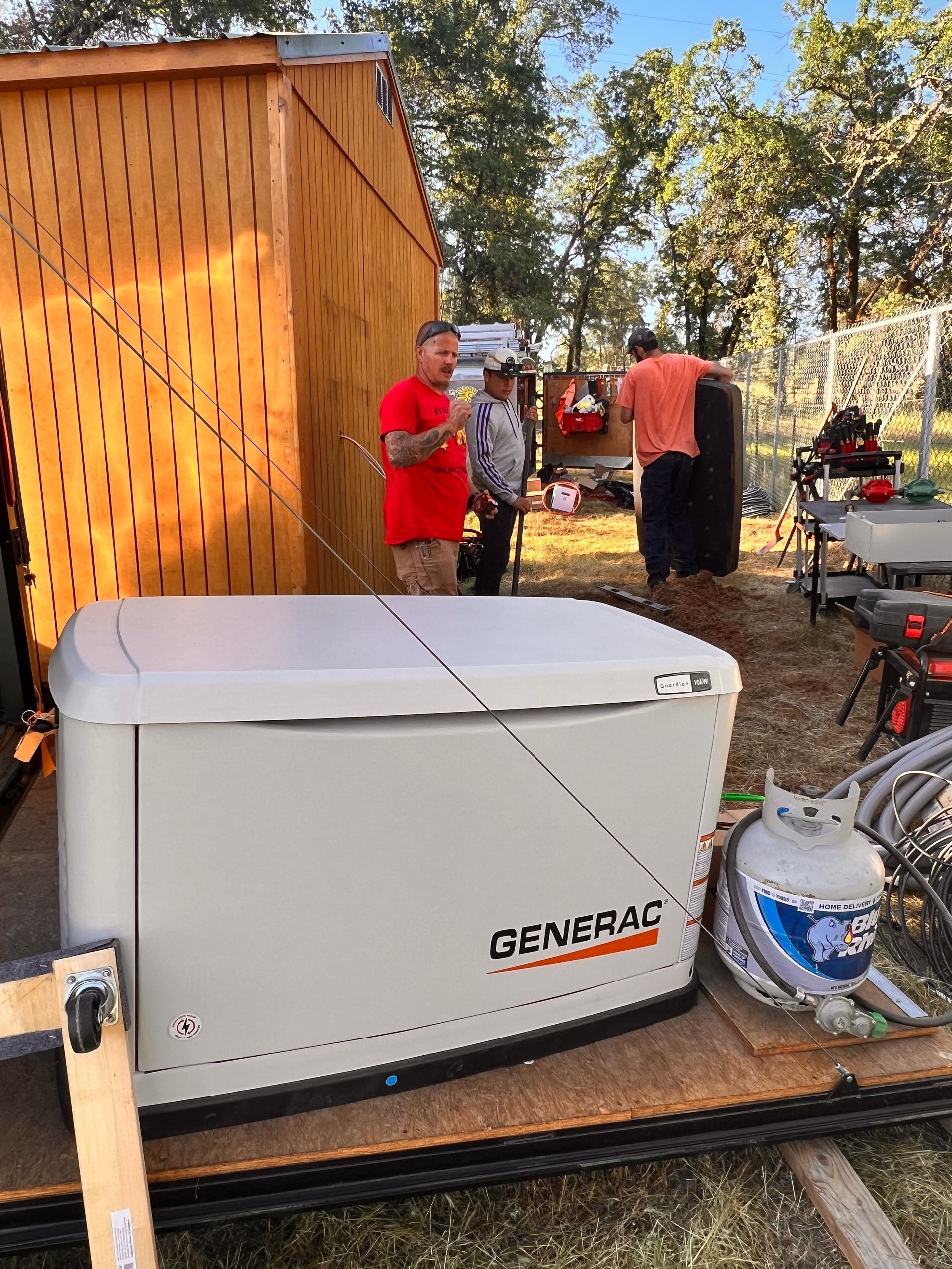 Workers installing a large Generac standby backup power generator outdoors near a residential shed.
