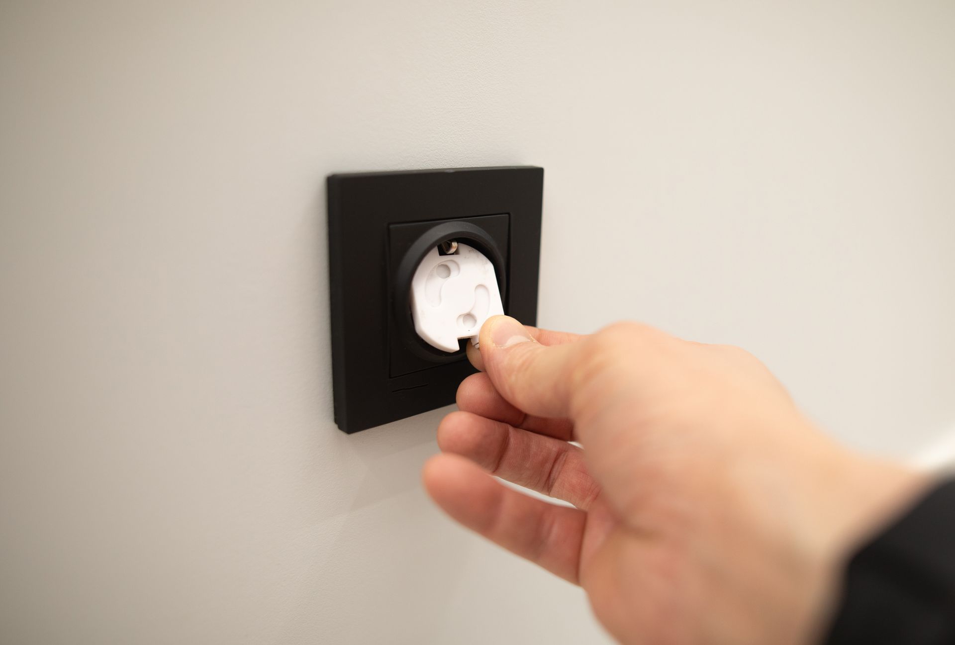 hand installing a white plastic child safety plug cover into a black electrical outlet.