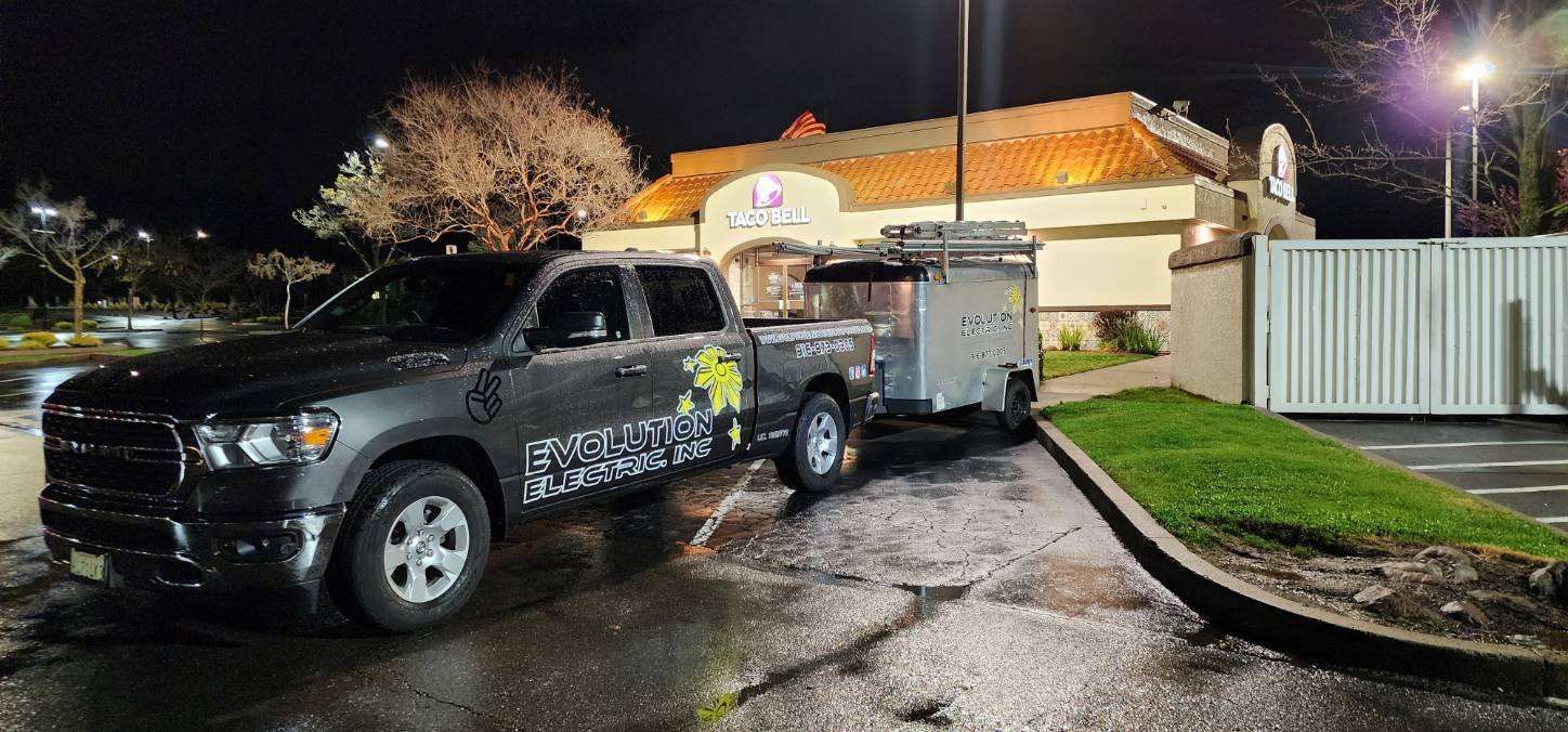 A truck and trailer are parked in front of a restaurant at night.