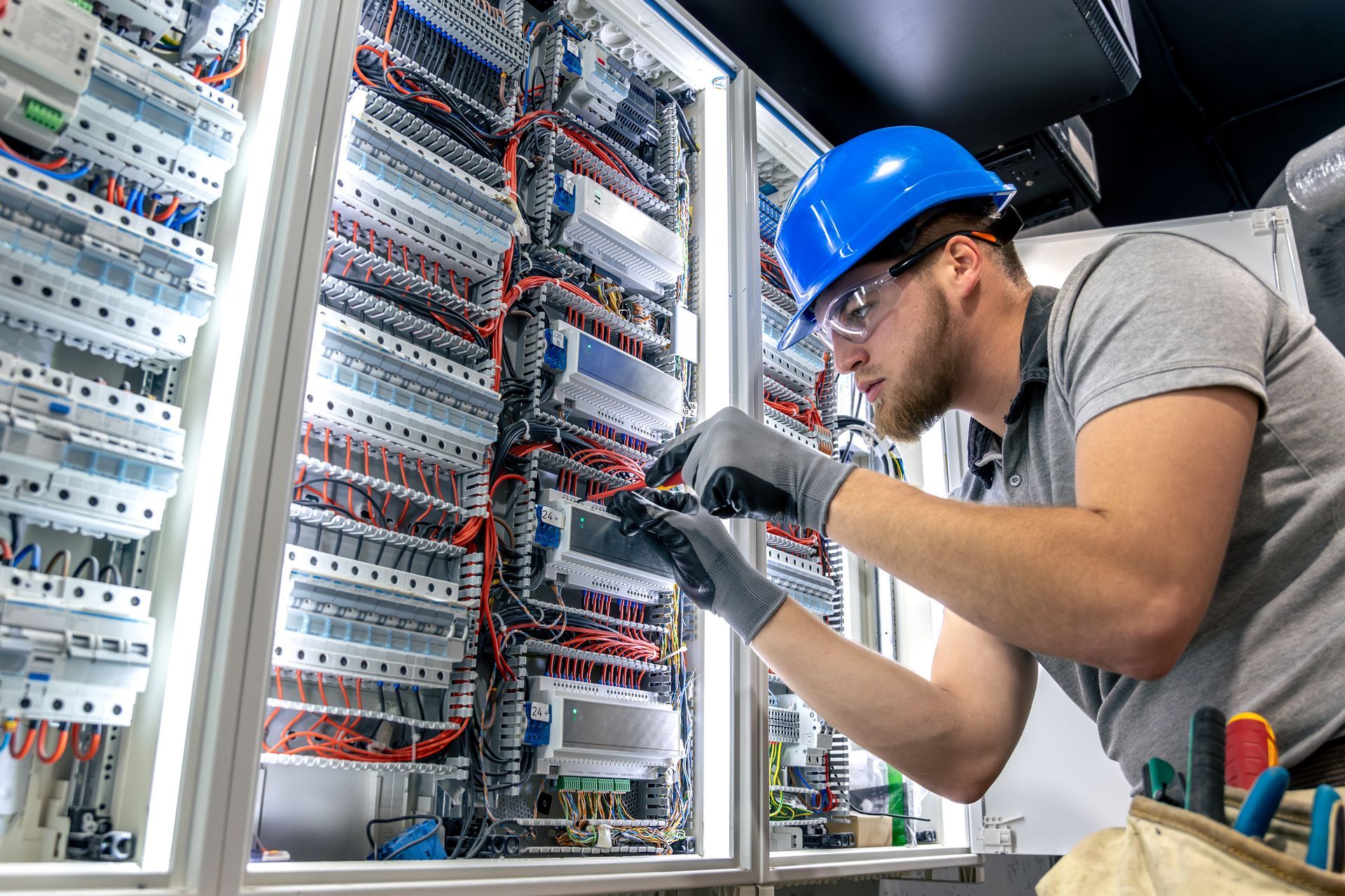 Electrician in a blue hard hat working on electrical panel wiring.