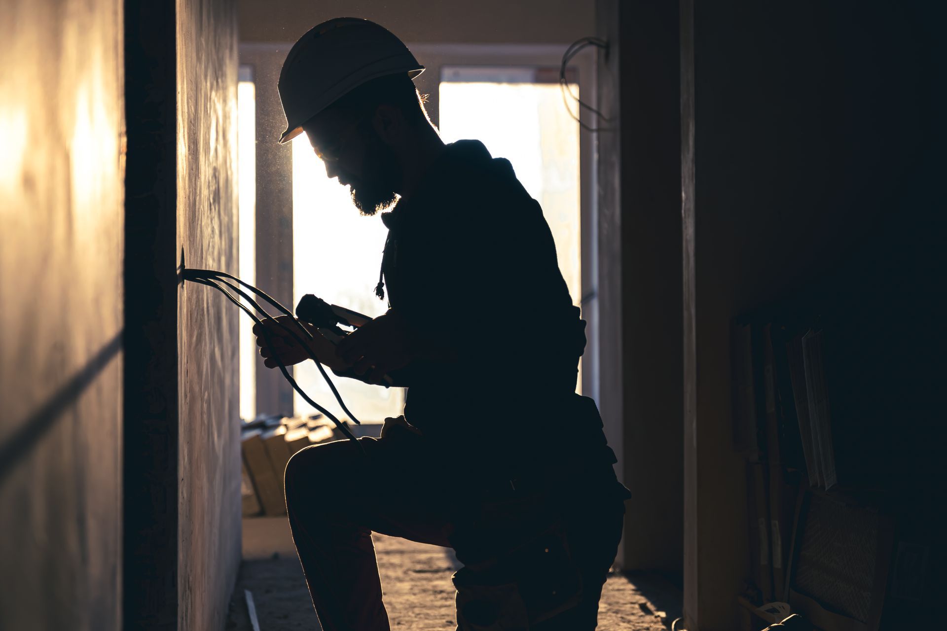 Electrician in silhouette, working on wires in a doorway, wearing a hard hat.
