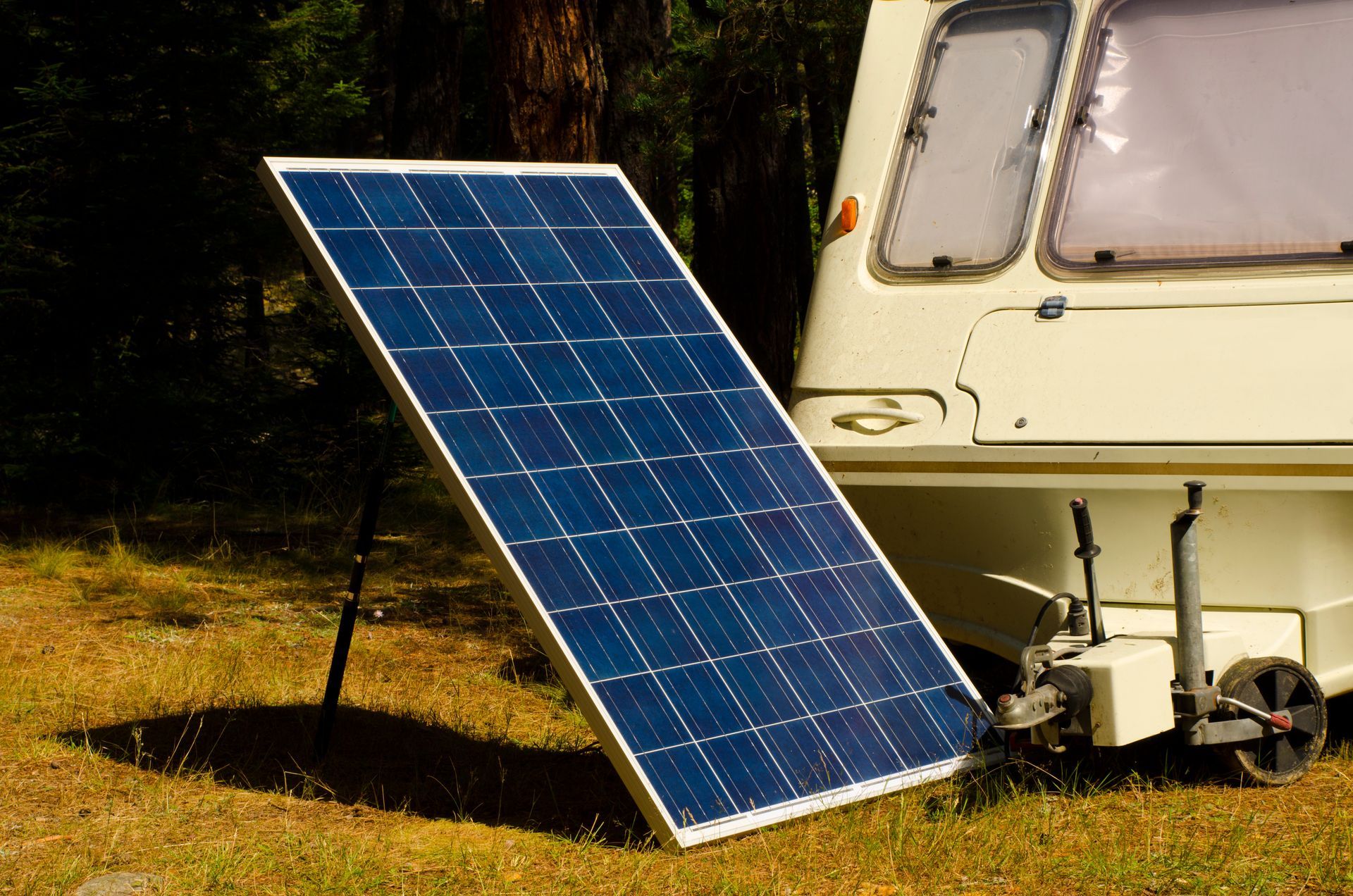 Solar panel leaning against a white camper van, on a grassy ground.
