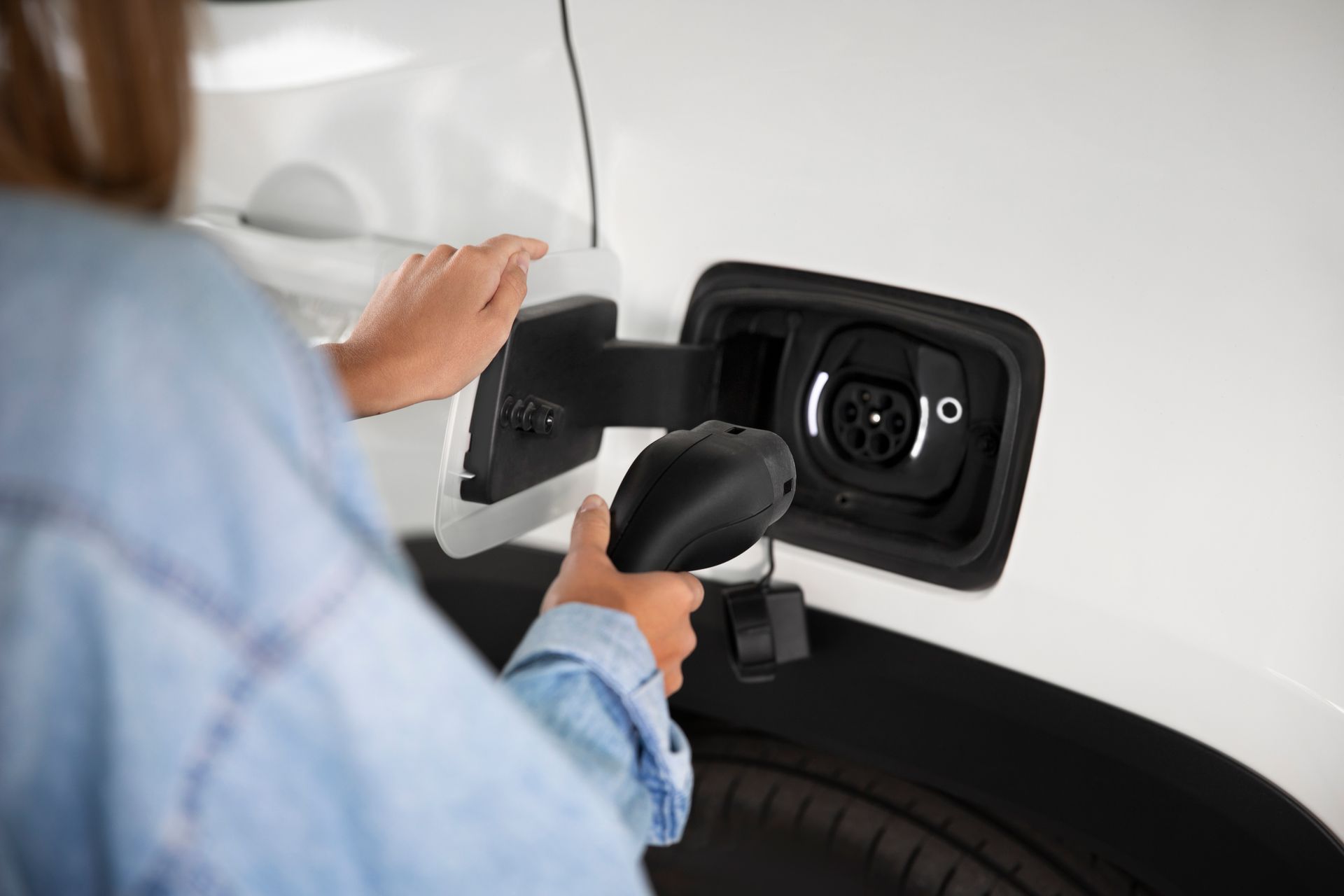 Person plugging an electric vehicle charging cable into a car's charging port.