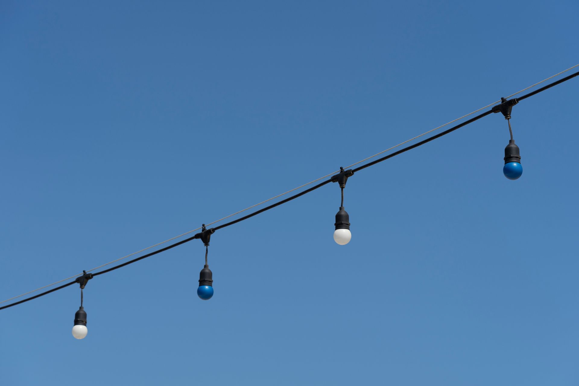 String of decorative lights against a clear blue sky, alternating white and blue bulbs.