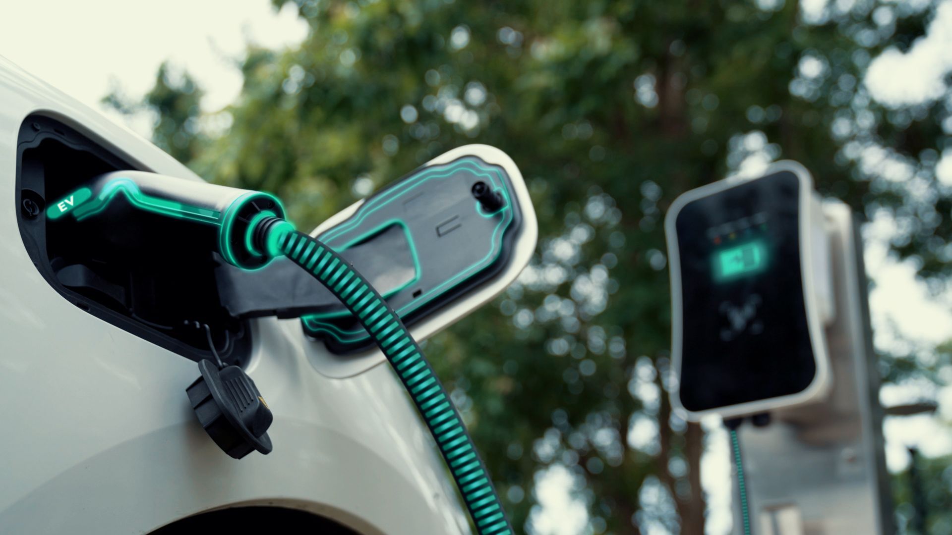 White electric car charging from a green-glowing charger at an outdoor charging station.