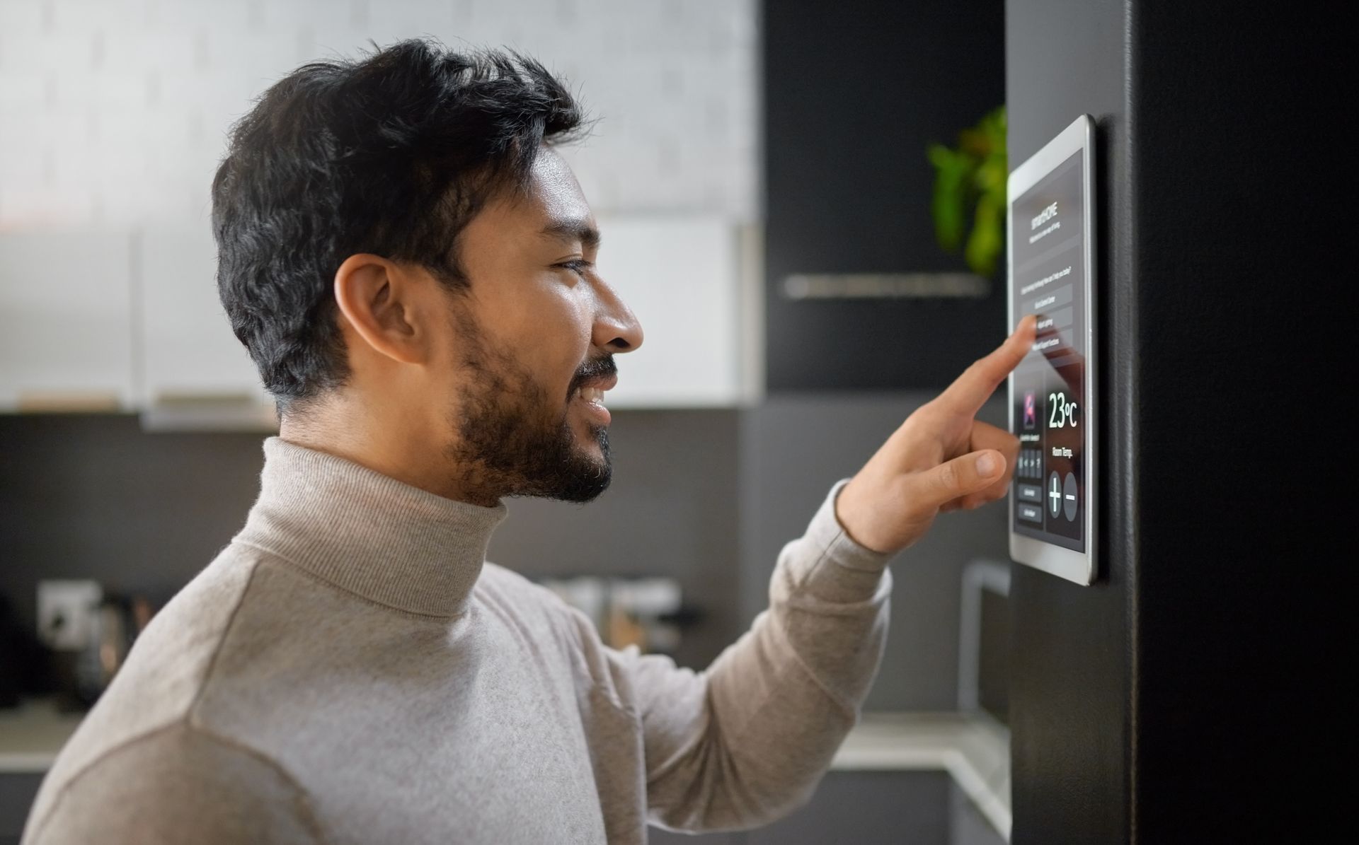 Man in turtleneck using a touchscreen tablet on a black wall in a kitchen.