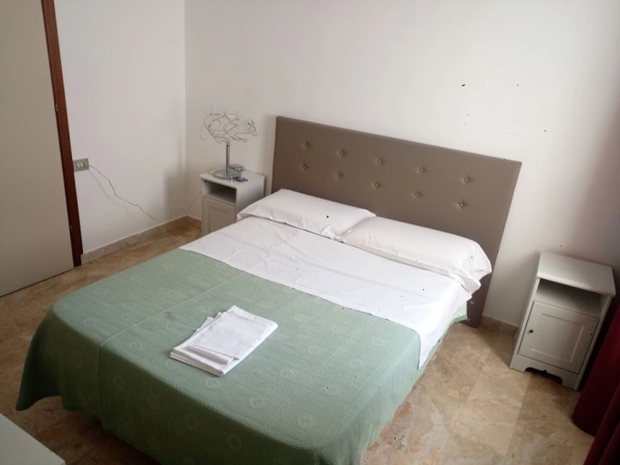 Un letto ben rifatto con coperta verde e lenzuola bianche in una semplice camera da letto con due comodini.