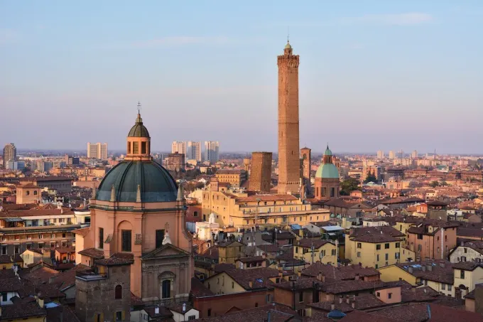 Panorama di Bologna con le due torri e la chiesa a cupola al tramonto.
