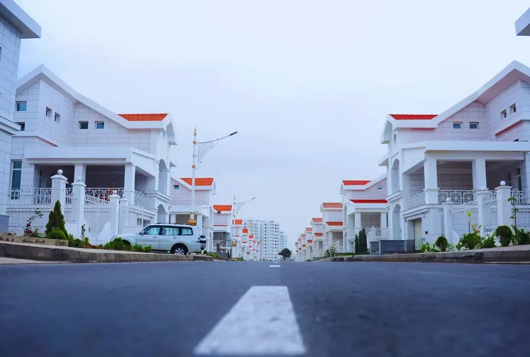 A white car is parked on the side of the road in front of a row of houses.