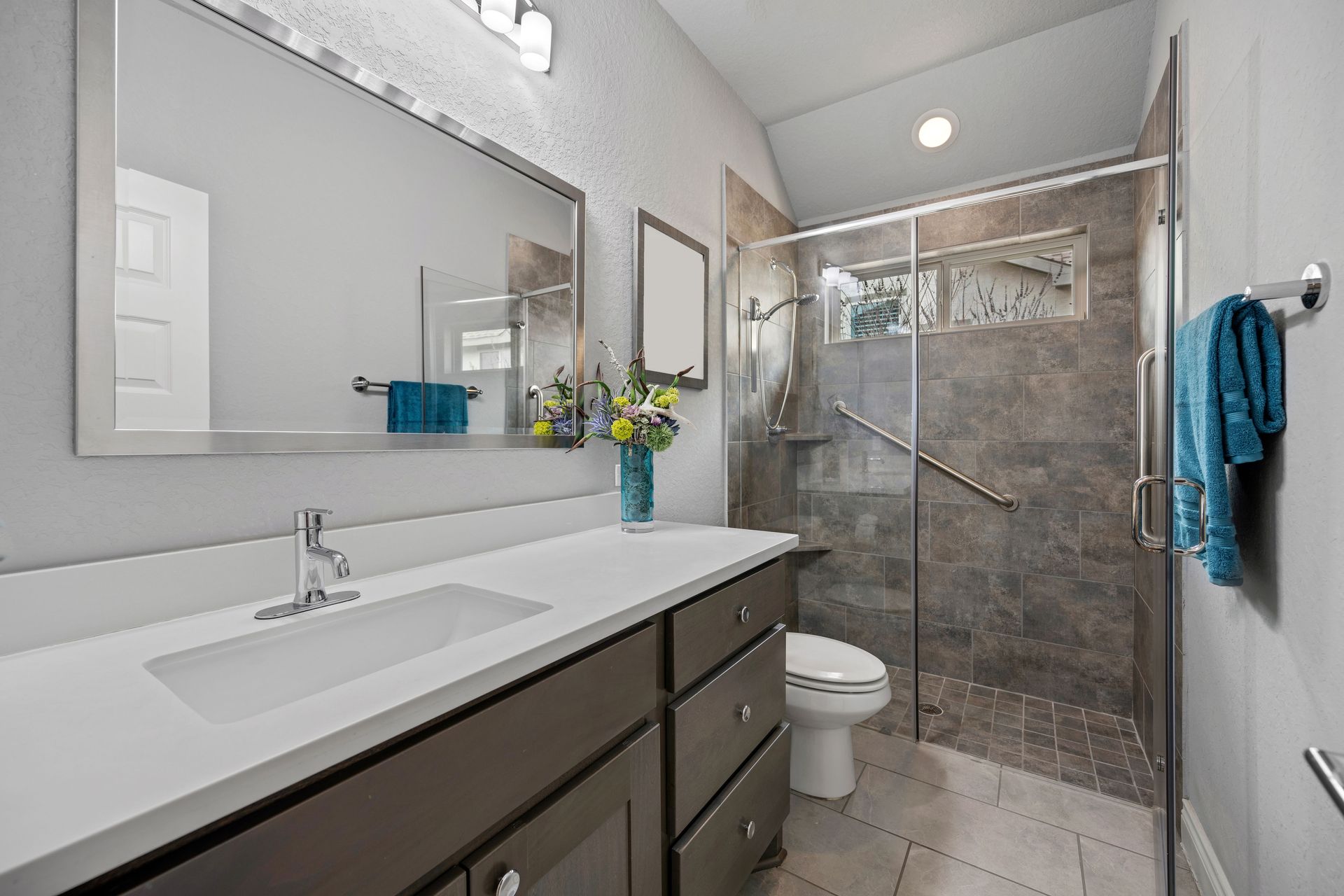 A bathroom with a sink , toilet , mirror and walk in shower.