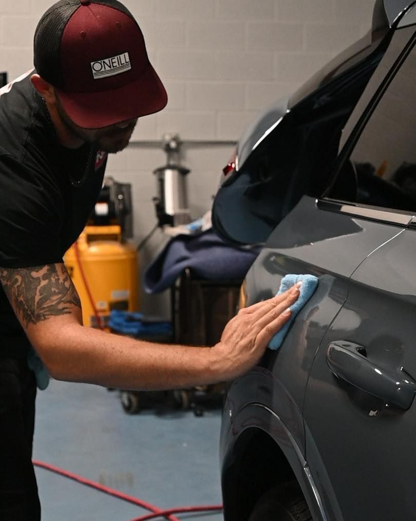 Man applying film to a car bumper with tools in a garage.