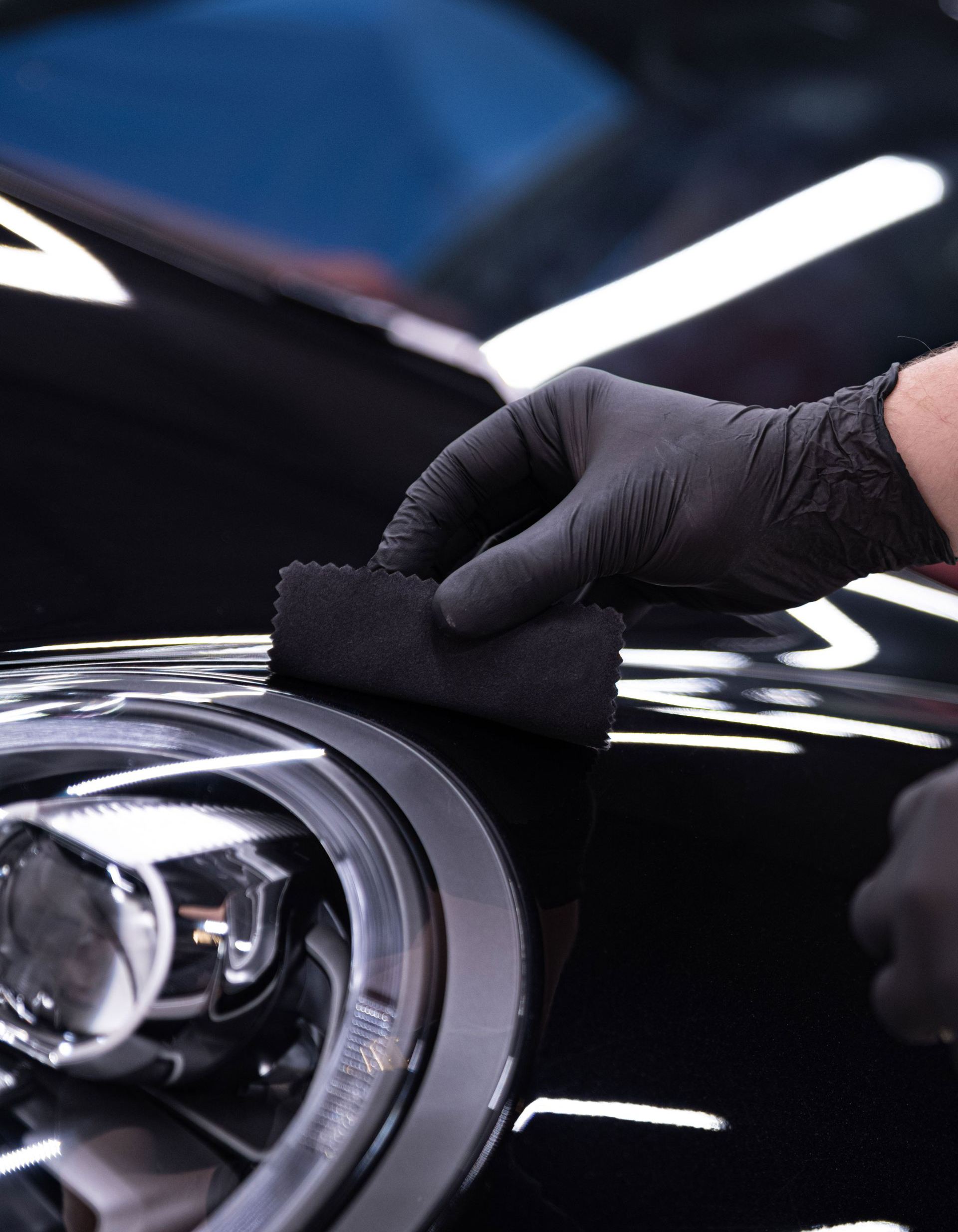 A person wearing black gloves applying a black coating to a car's headlight.