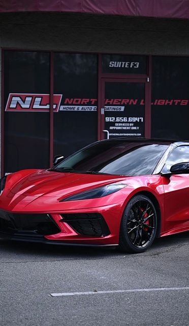 Red sports car parked outside a tuning shop with black and red signage.