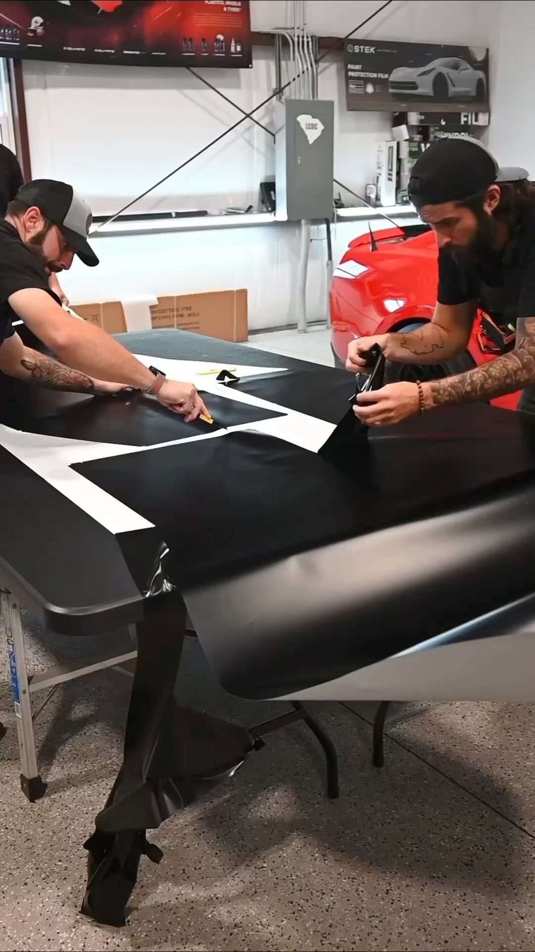 Yellow car with black spoiler in front of a red car and other cars inside a garage.