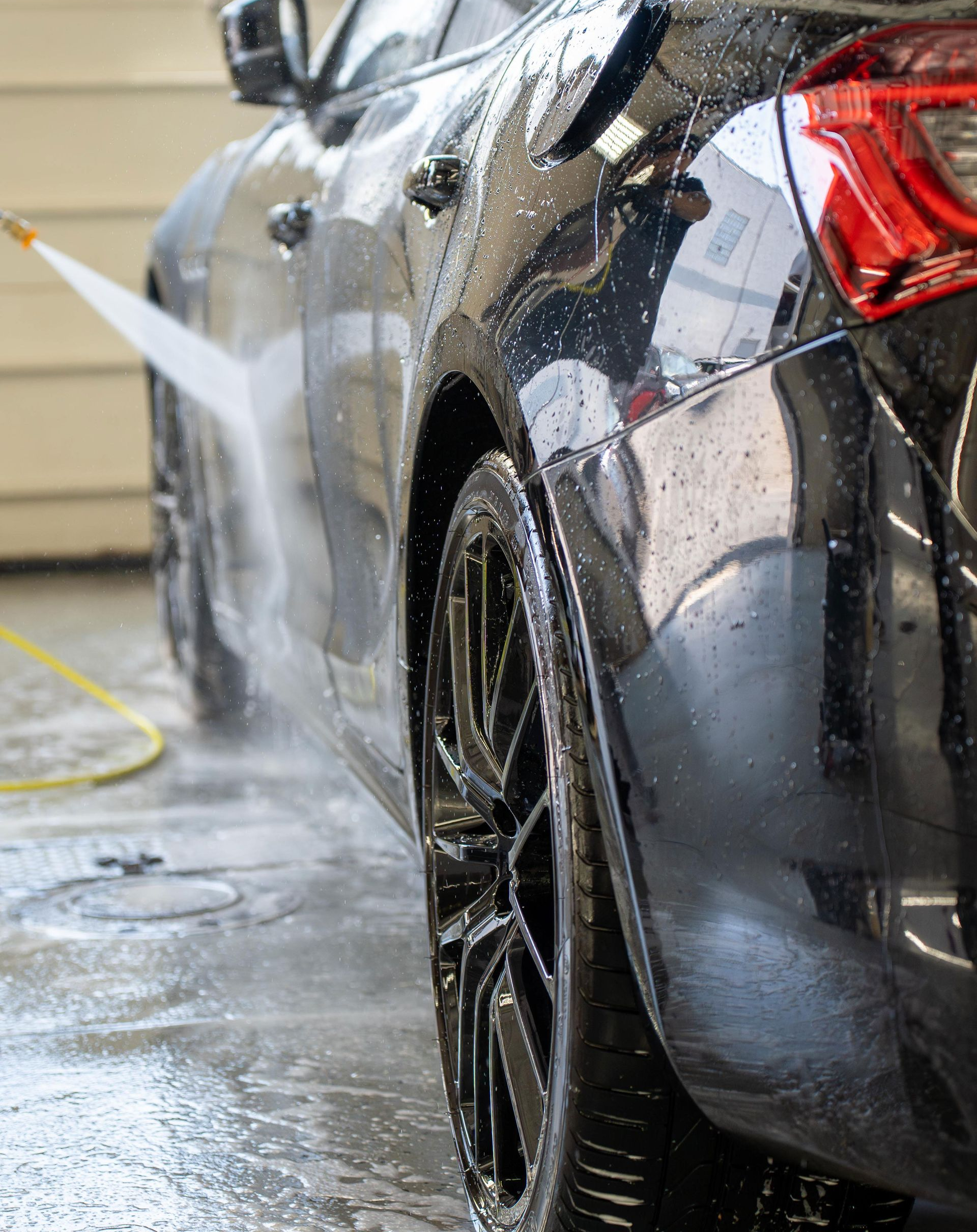 Black car being washed with a pressure washer, water spraying on the side and tire.