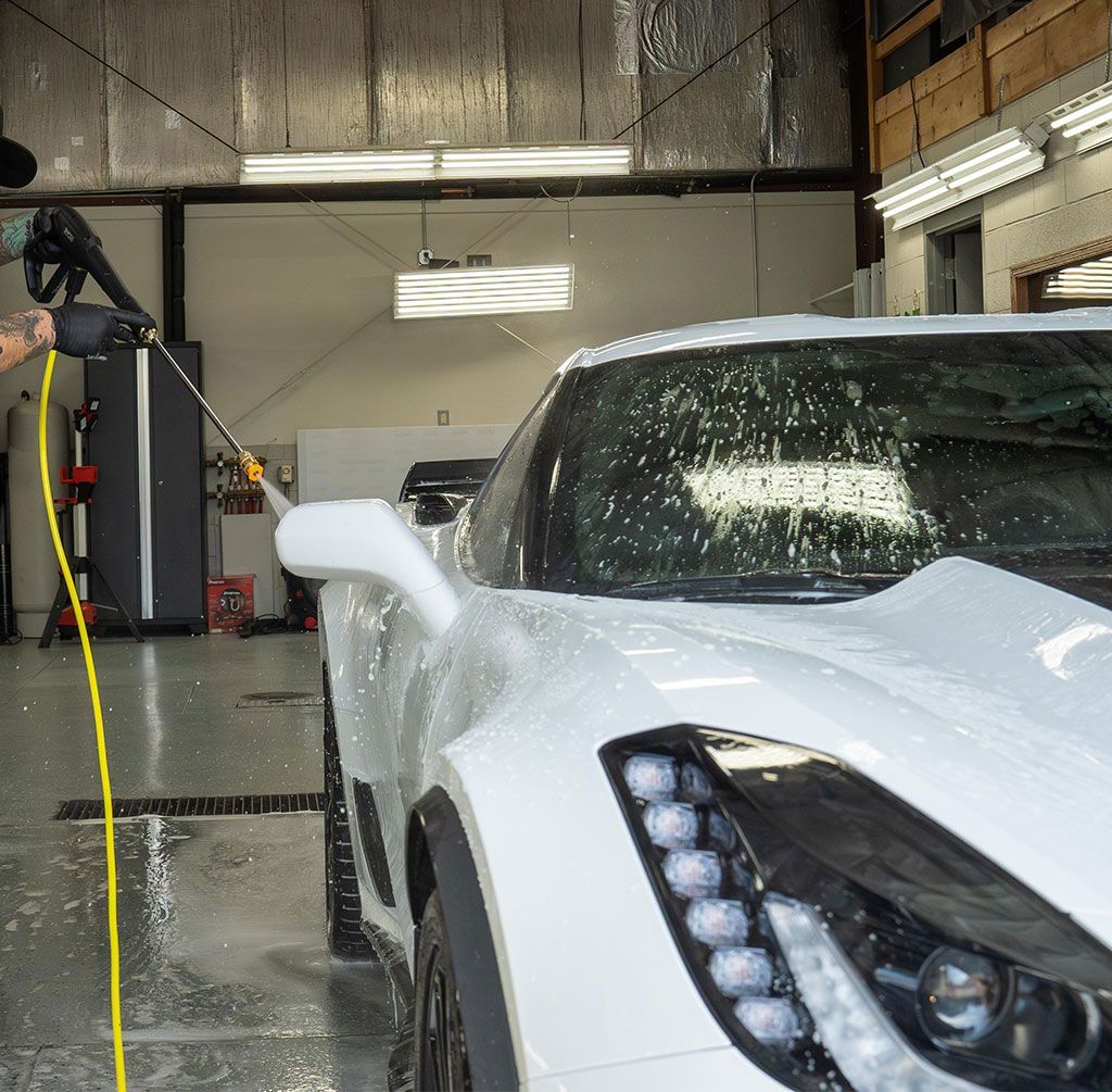 White sports car being washed with a pressure washer in a garage.