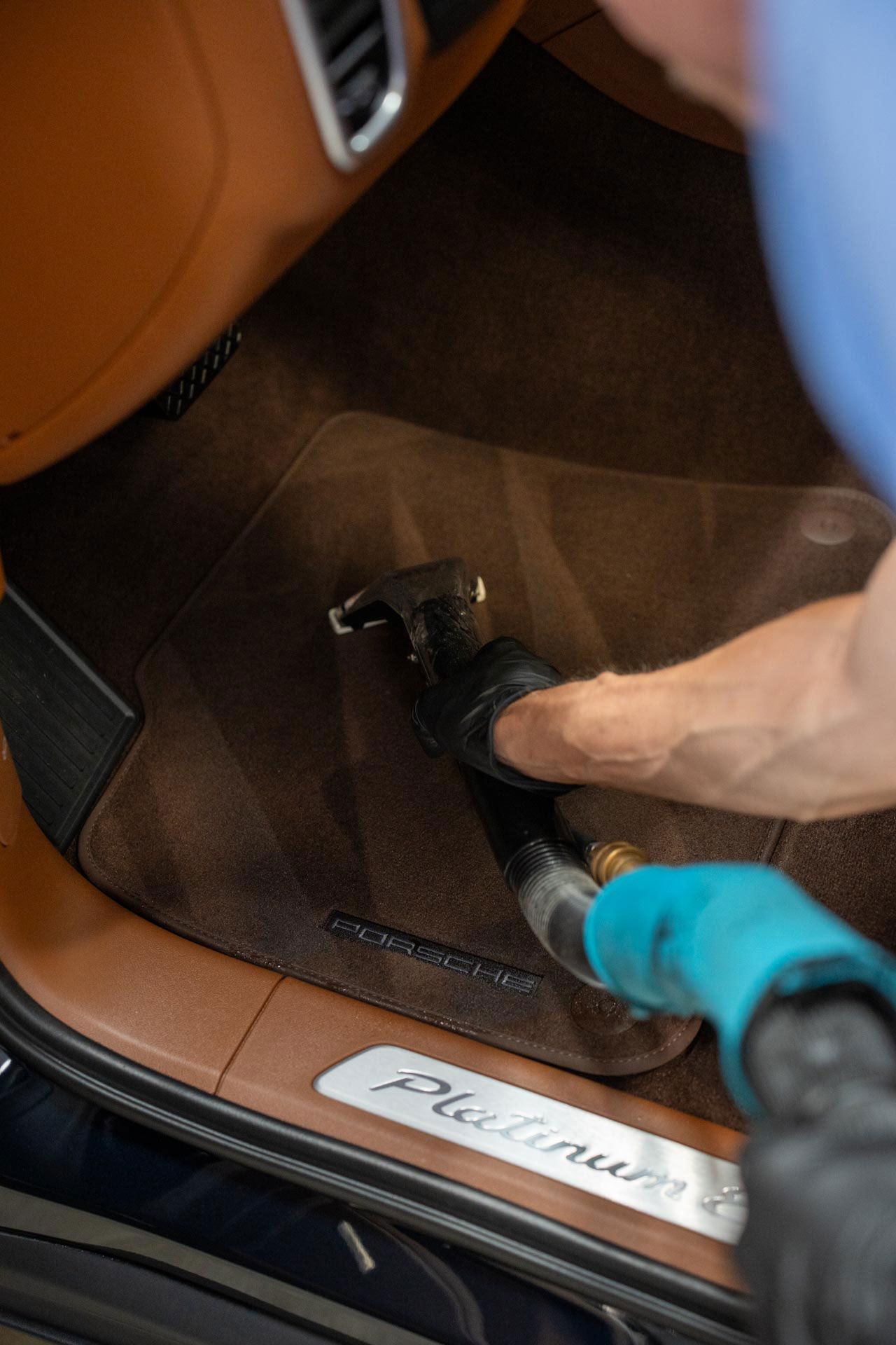 A person vacuuming a car's brown carpet floor mat;