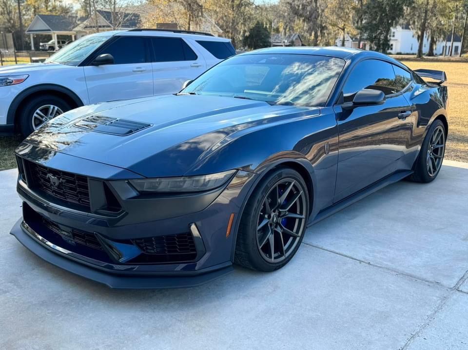 a black mustang is parked in a driveway next to a white suv .