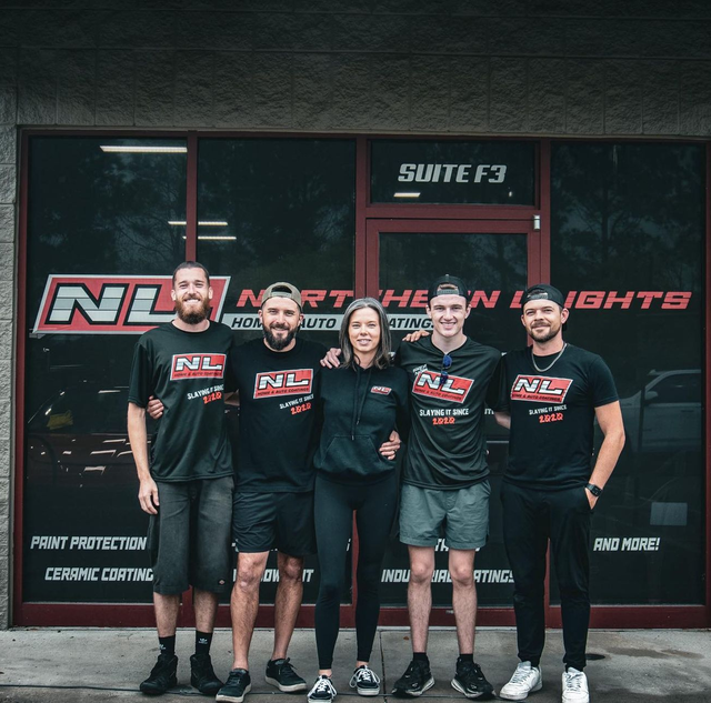Five people in matching team uniforms stand outside a storefront with 