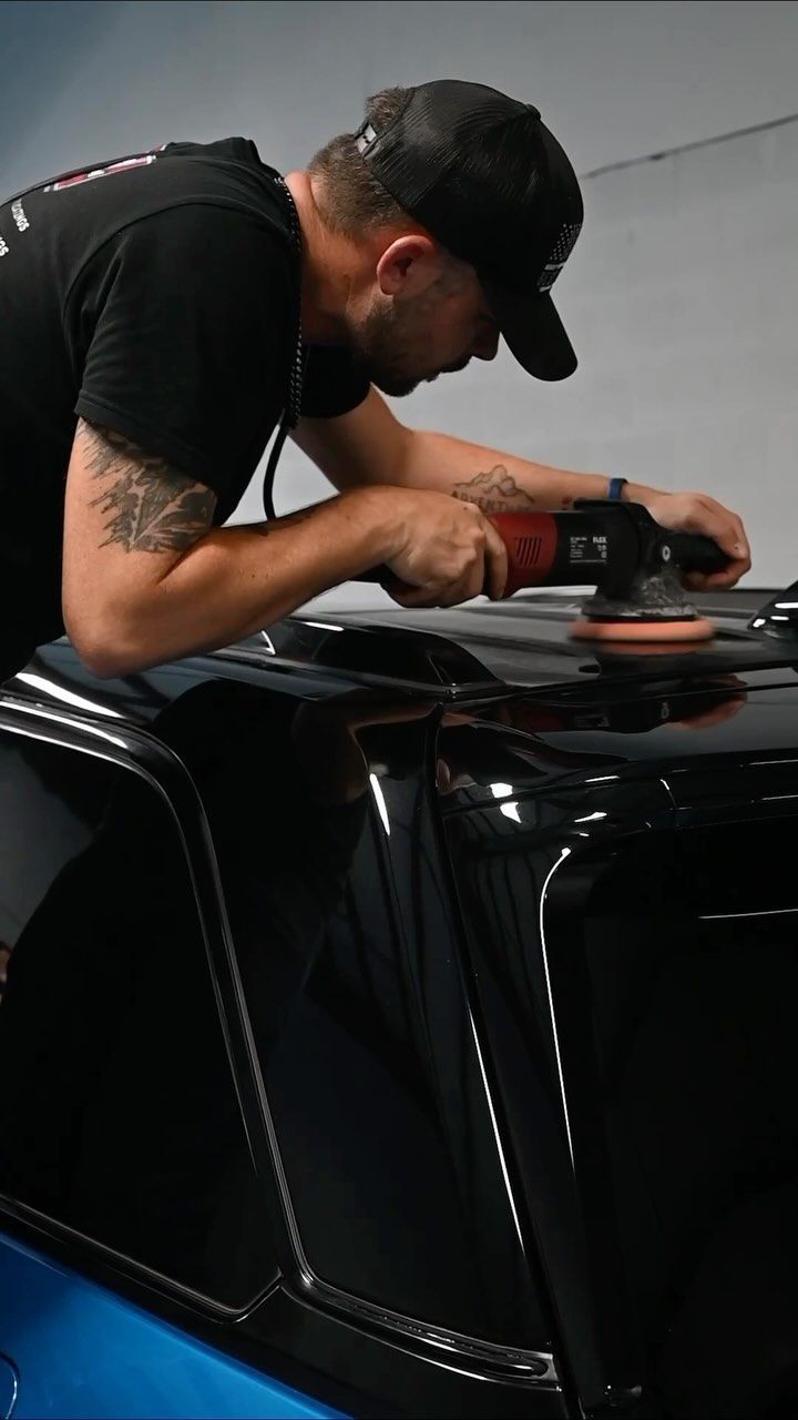 Man using a power buffer on a black car roof. He's wearing a baseball cap and has tattoos on his arm.