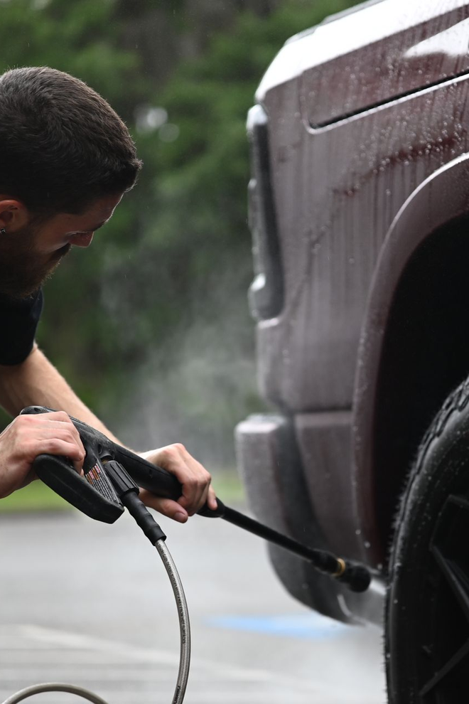 Close-up of a dark SUV wheel and fender being sprayed with water during a car wash