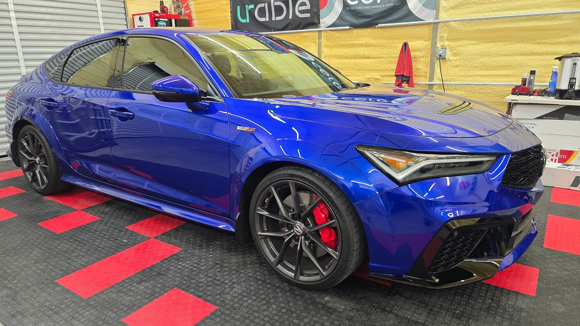 Blue Honda Integra car parked indoors, black rims, red brake calipers.