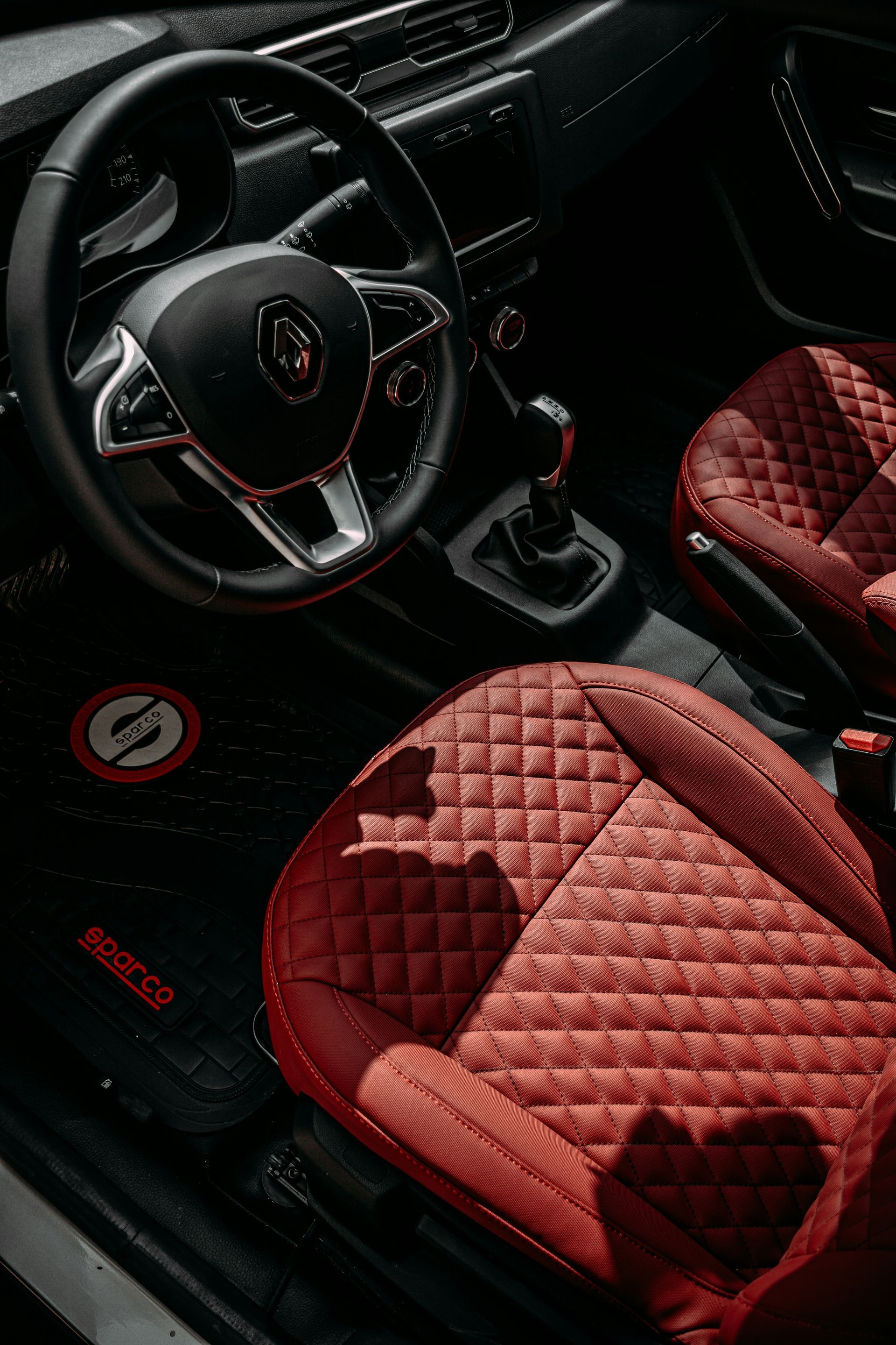 Red quilted car interior with black steering wheel and floor mats.