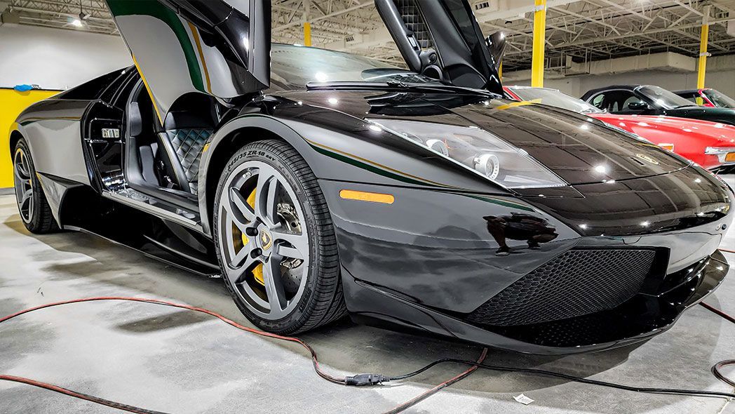 Black sports car with gull-wing doors open, on display in a brightly lit showroom.