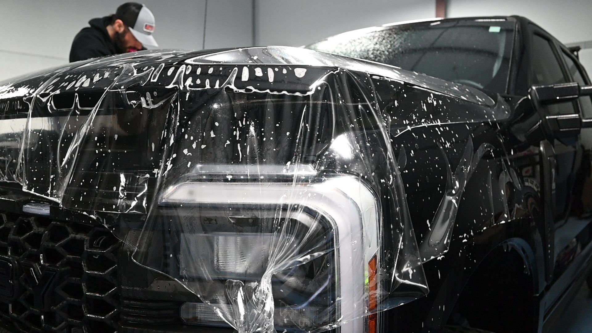 Trained technician stretching and positioning paint protection film on a vehicle.