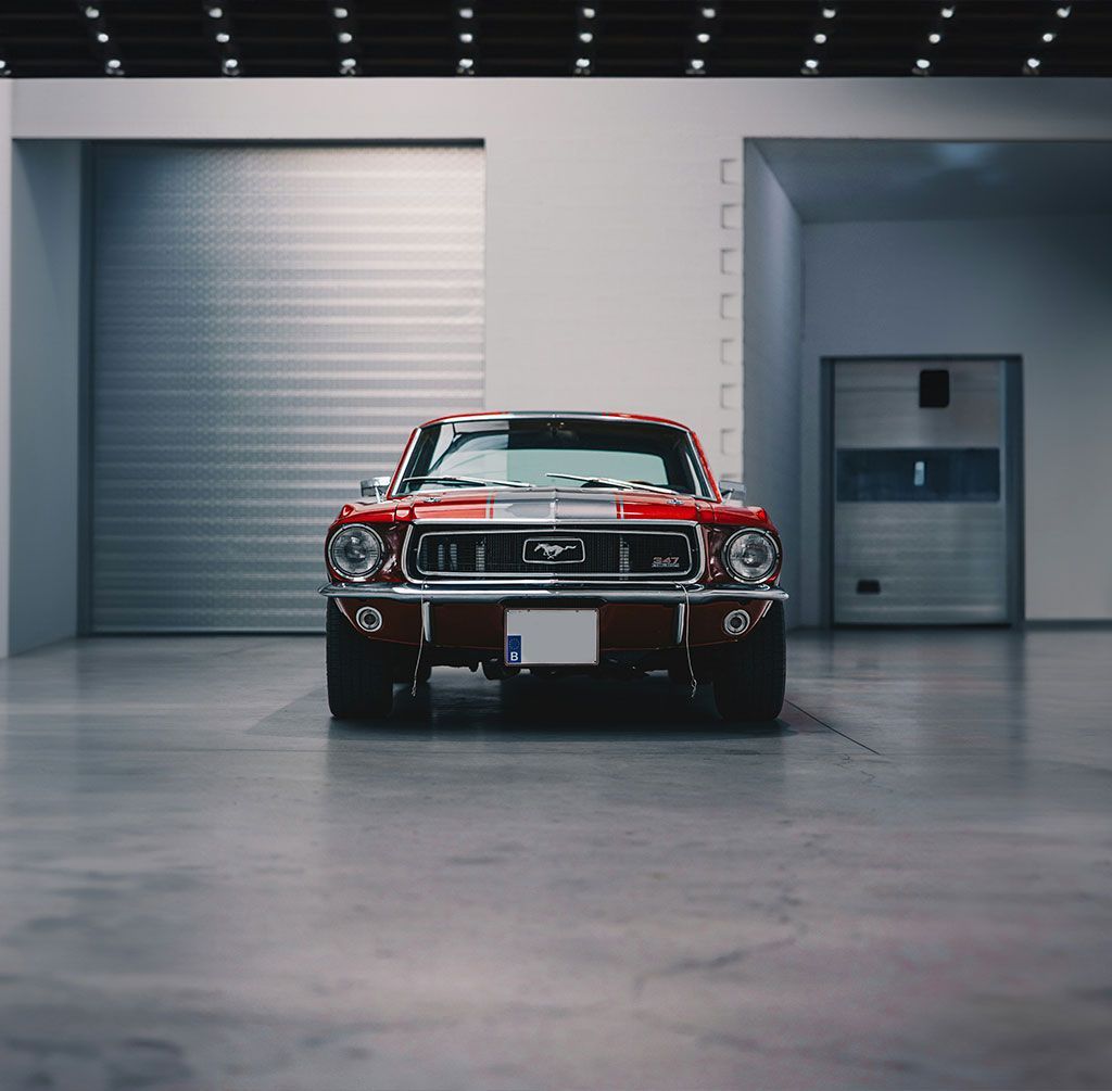 Red classic Mustang car inside a gray garage with overhead lighting.