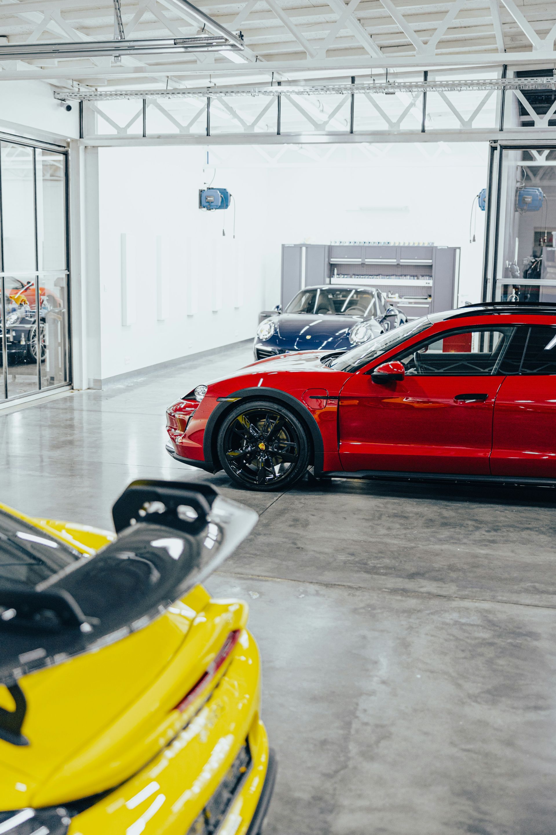 Yellow car with black spoiler in front of a red car and other cars inside a garage.