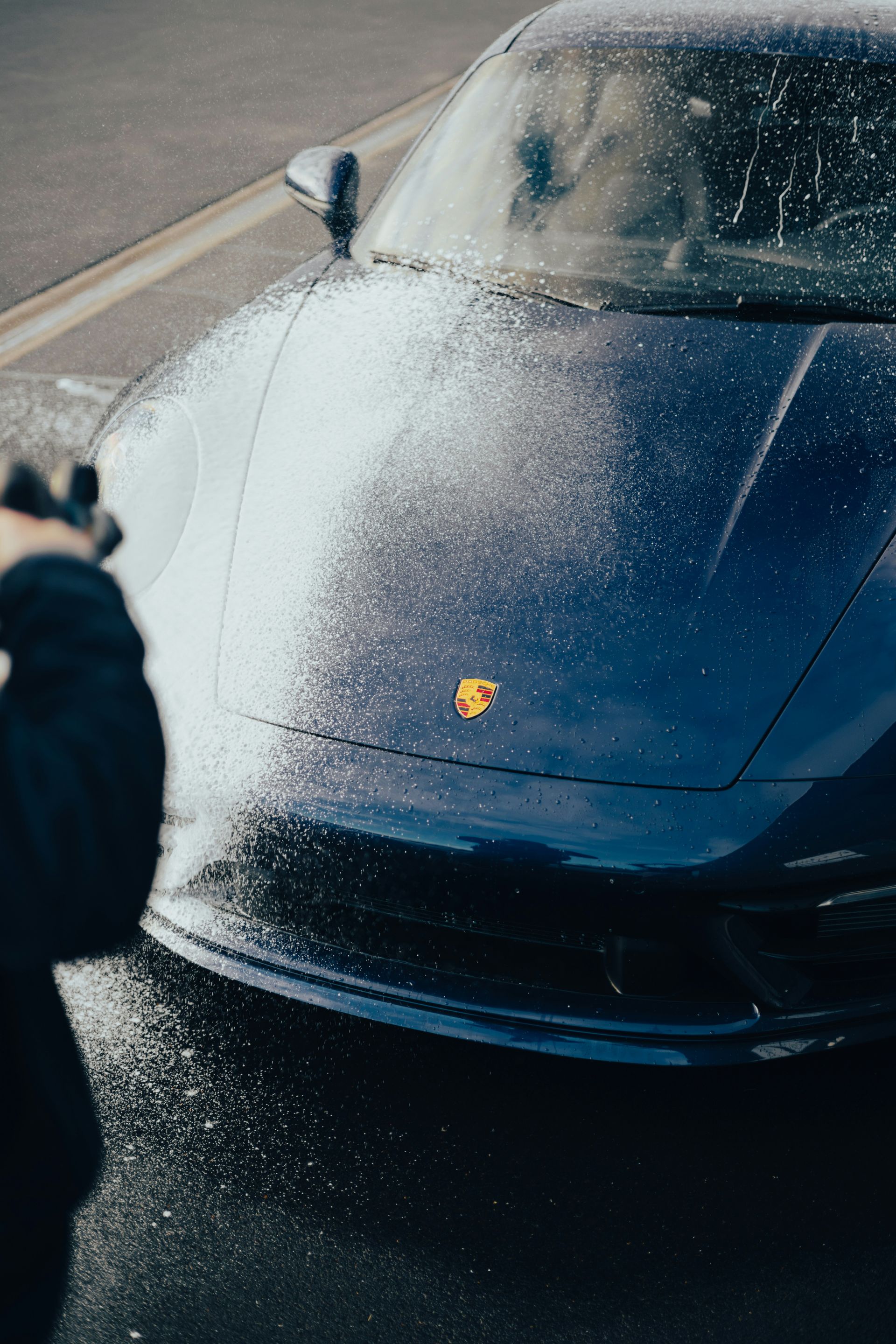 Blue car being sprayed with water; gold emblem visible on the hood.