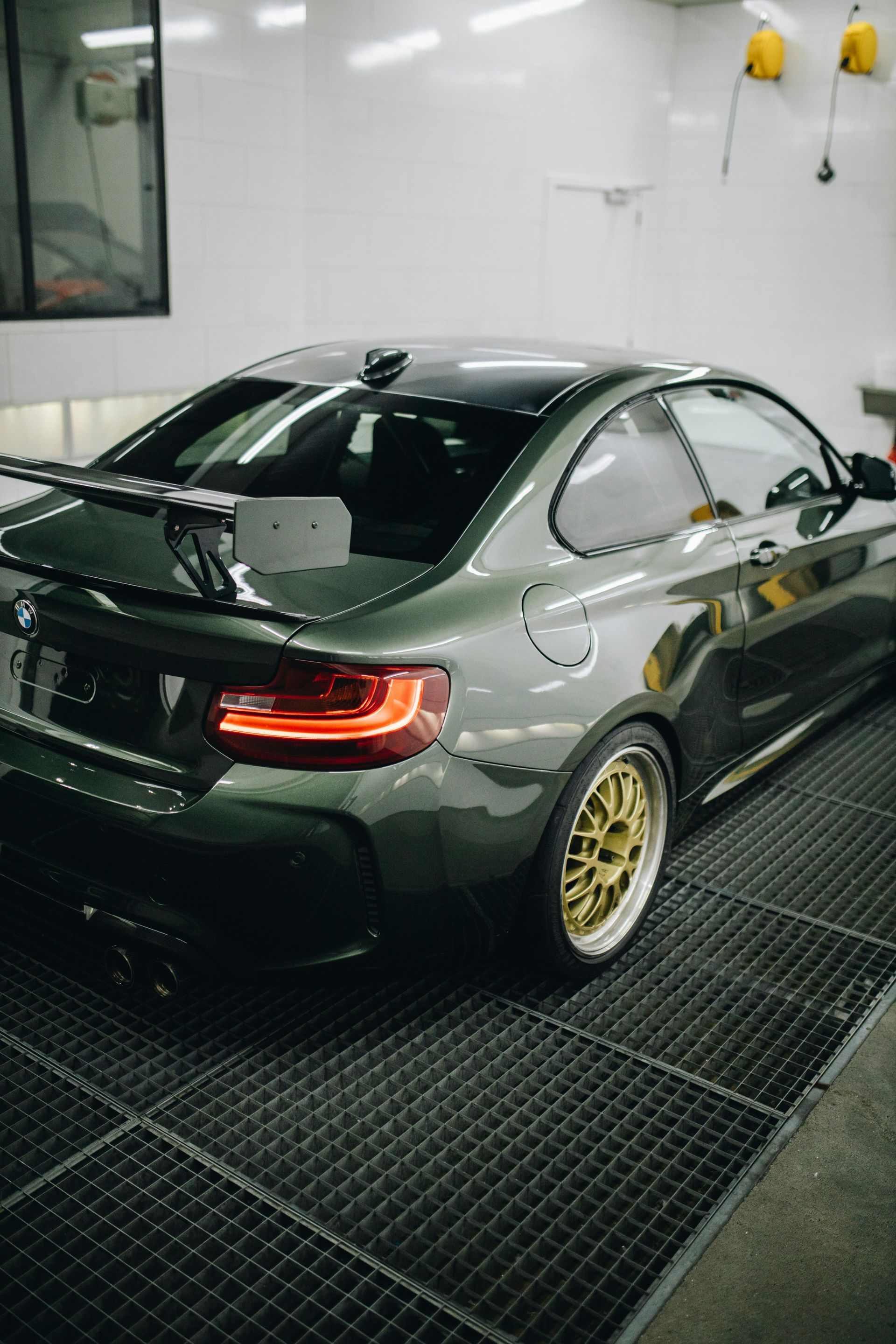 Green BMW coupe with gold rims, parked inside a garage.