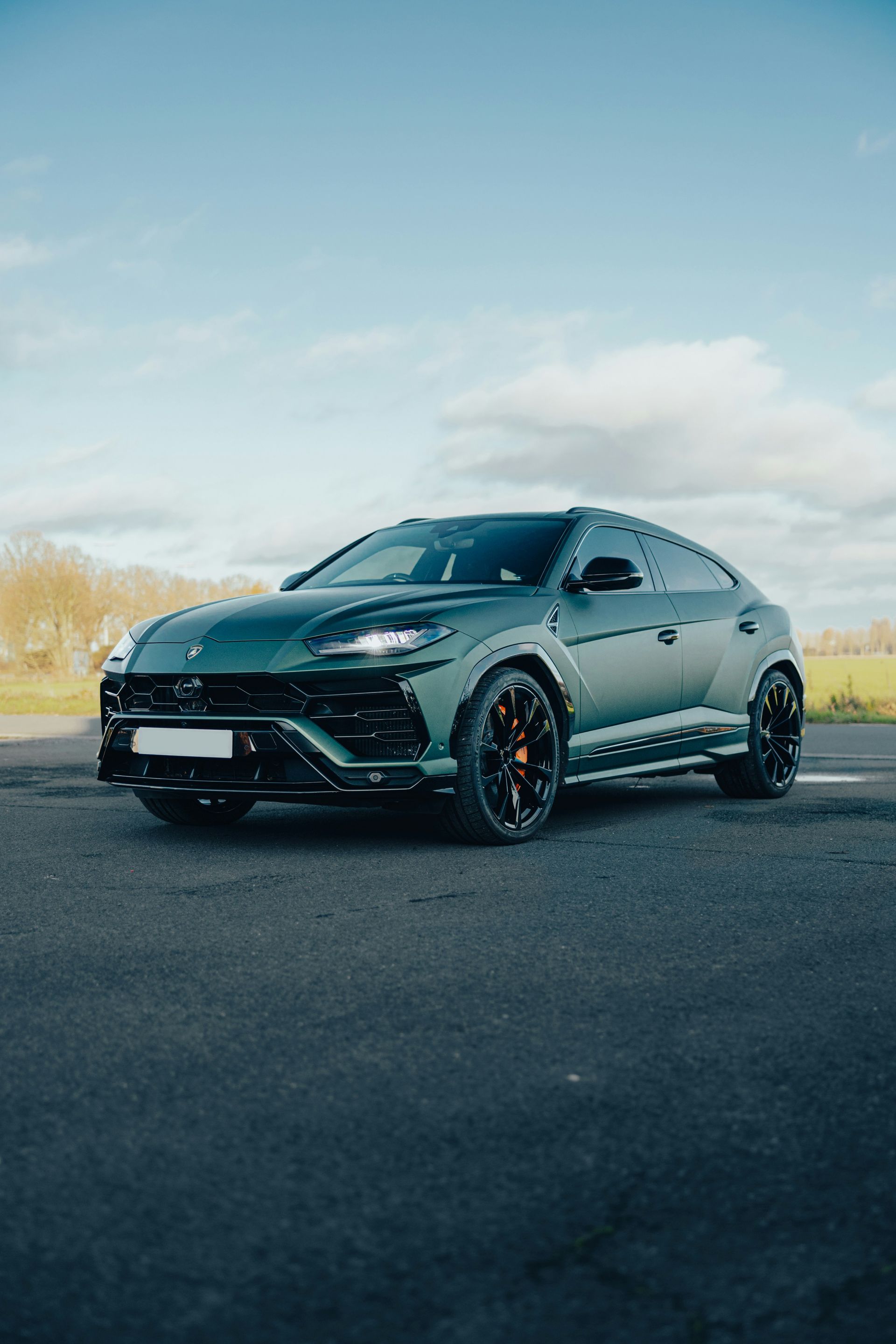 Green Lamborghini Urus SUV on a dark asphalt road under a blue sky.