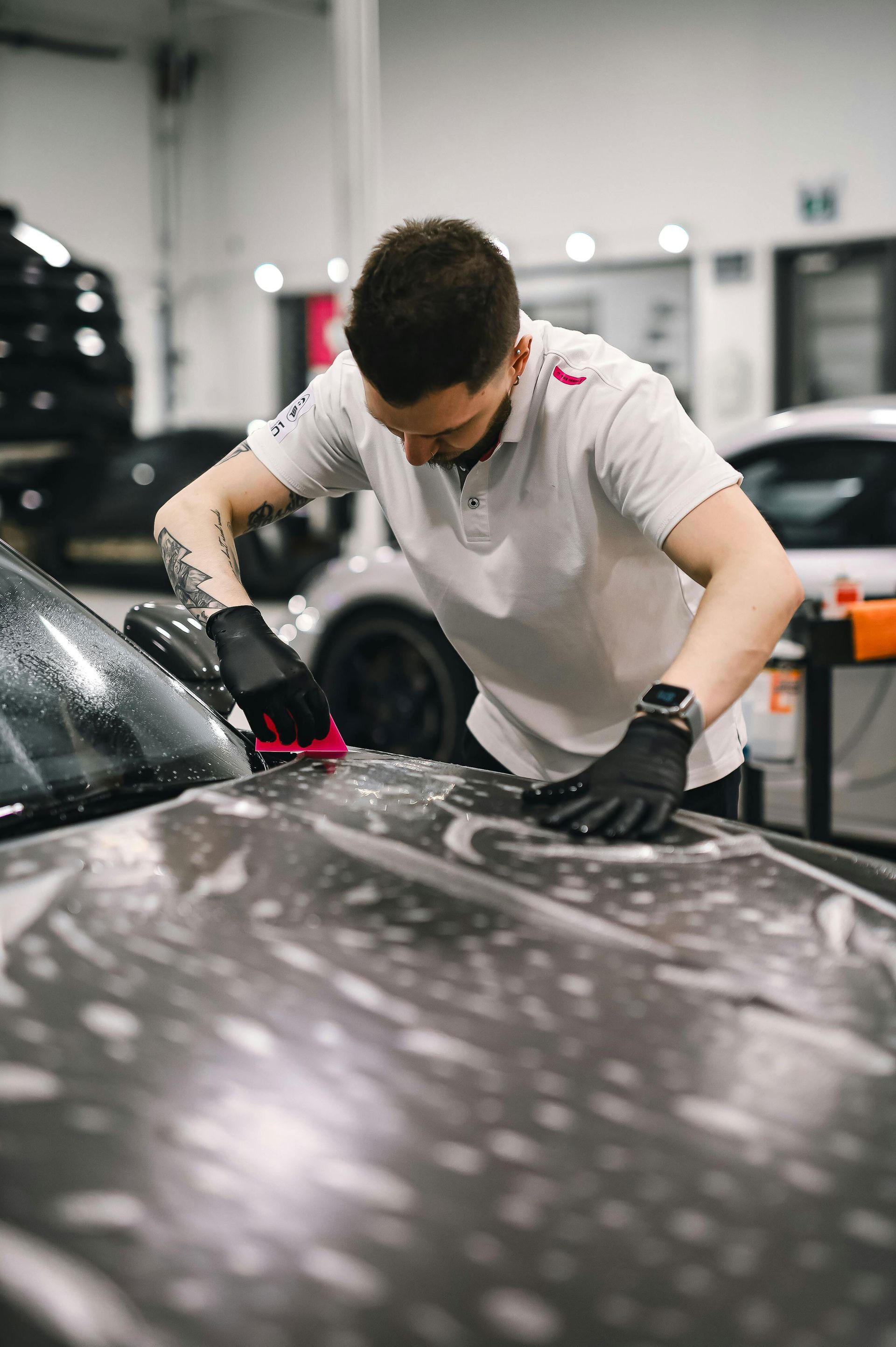 Man in a garage washing a car hood, applying soap with a squeegee.