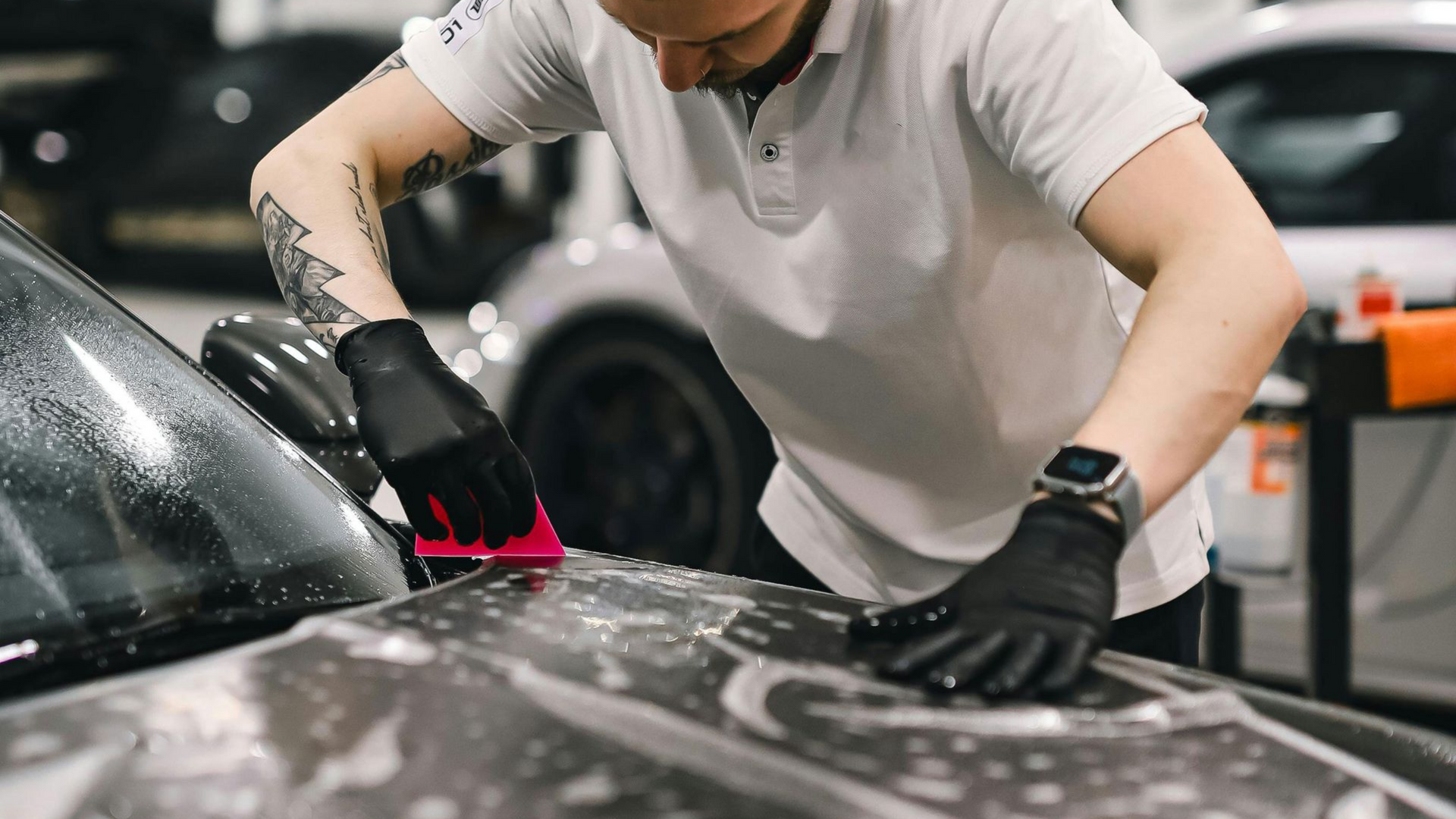 Man in black gloves applying film to car, indoors.