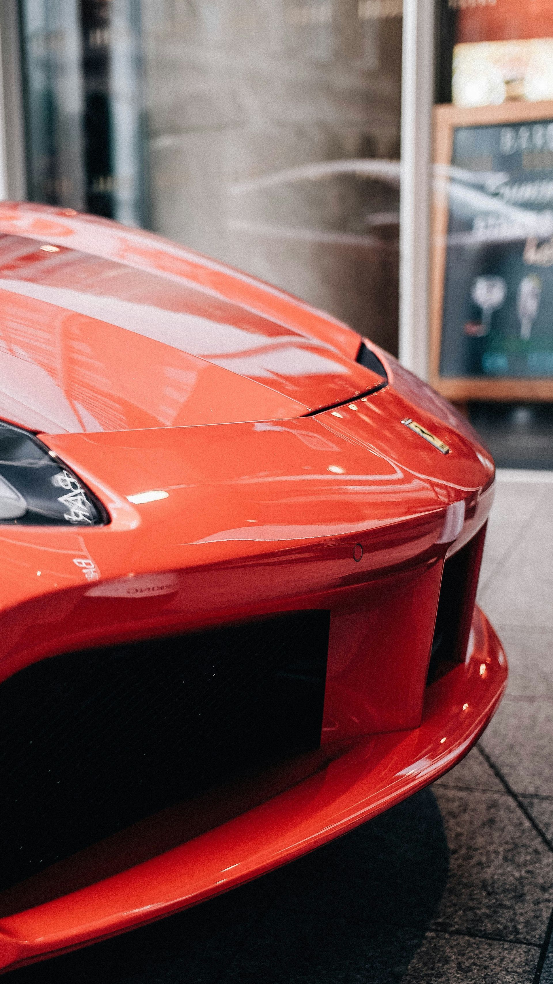 Red Ferrari sports car, close up of front, against a city backdrop.