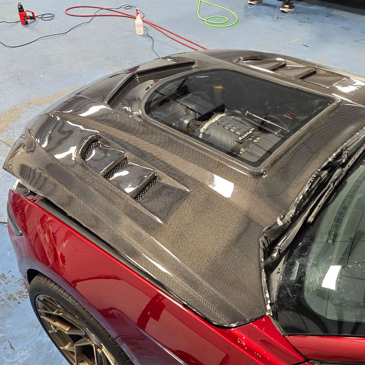 Carbon fiber car hood on a red car with an exposed engine bay.