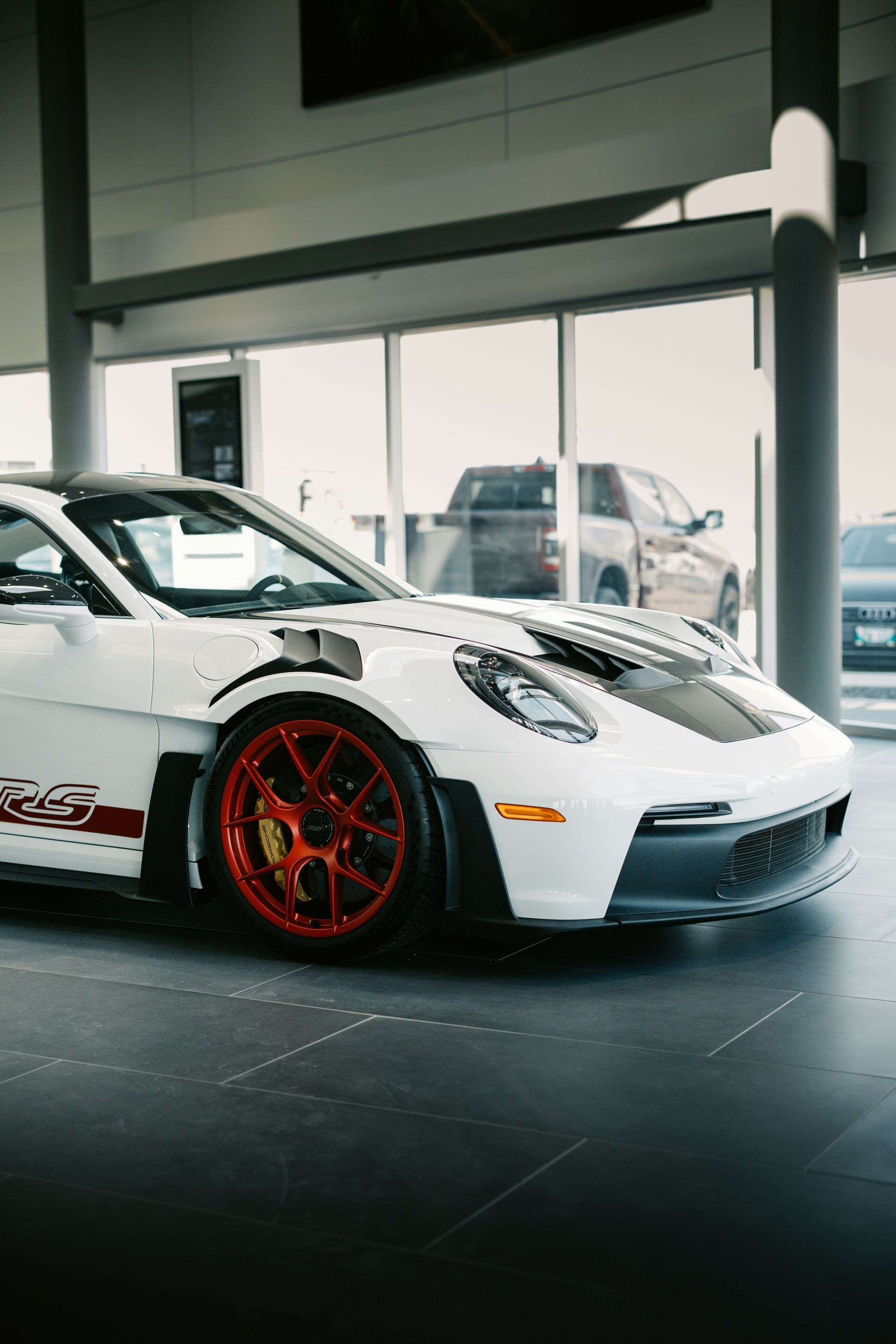 White Porsche GT3 with red wheels in a showroom.
