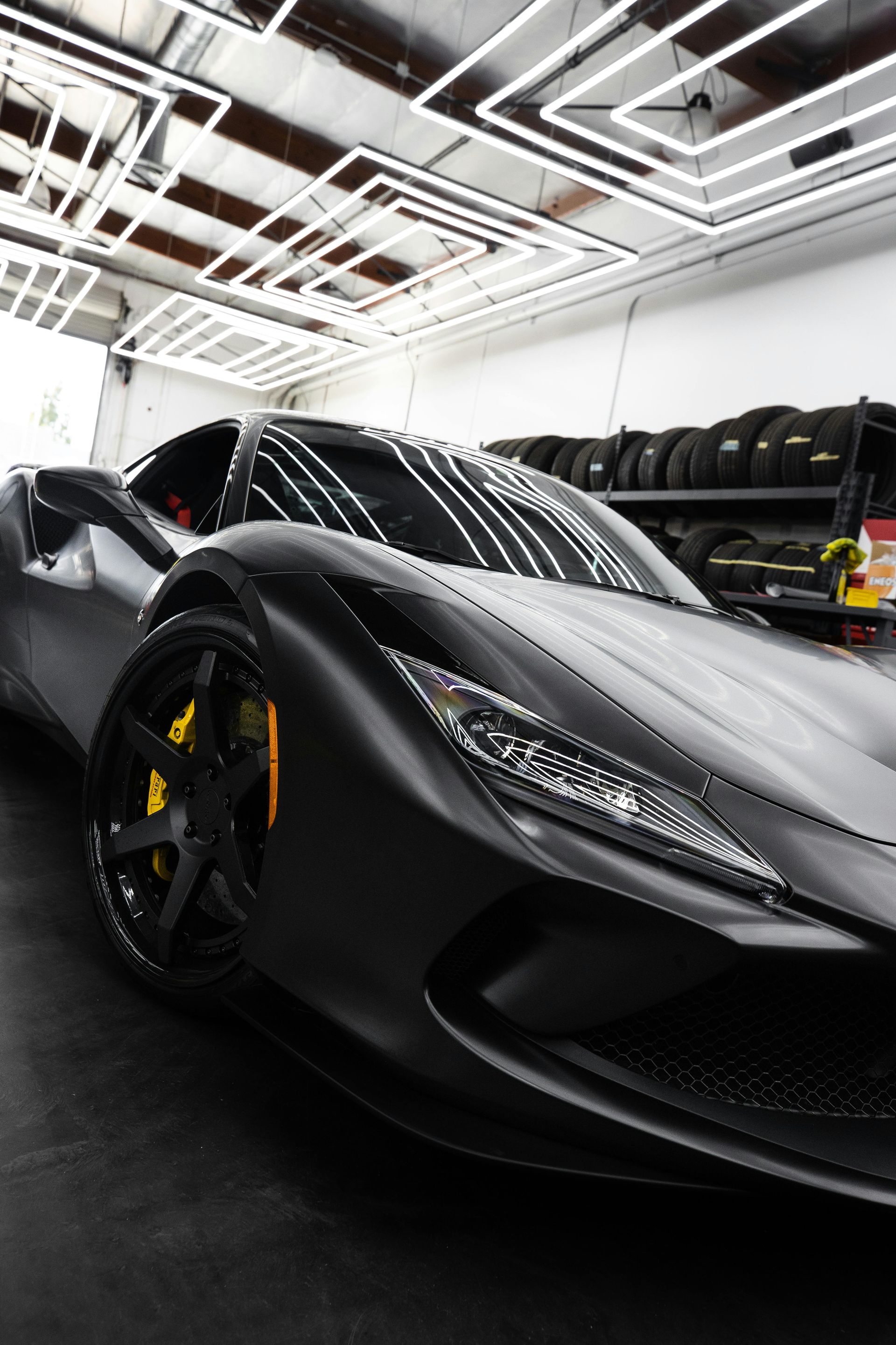 Black sports car in a brightly lit garage, with yellow brake calipers, and tires in the background.